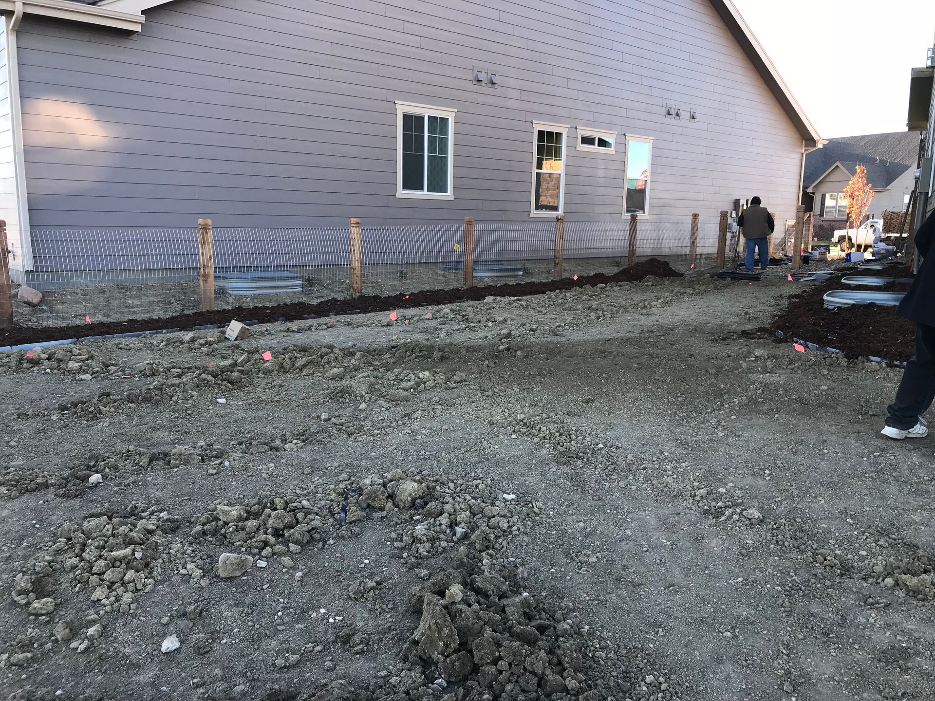 Construction site with house, dirt, gravel, posts, and workers. Exterior of a home under construction.