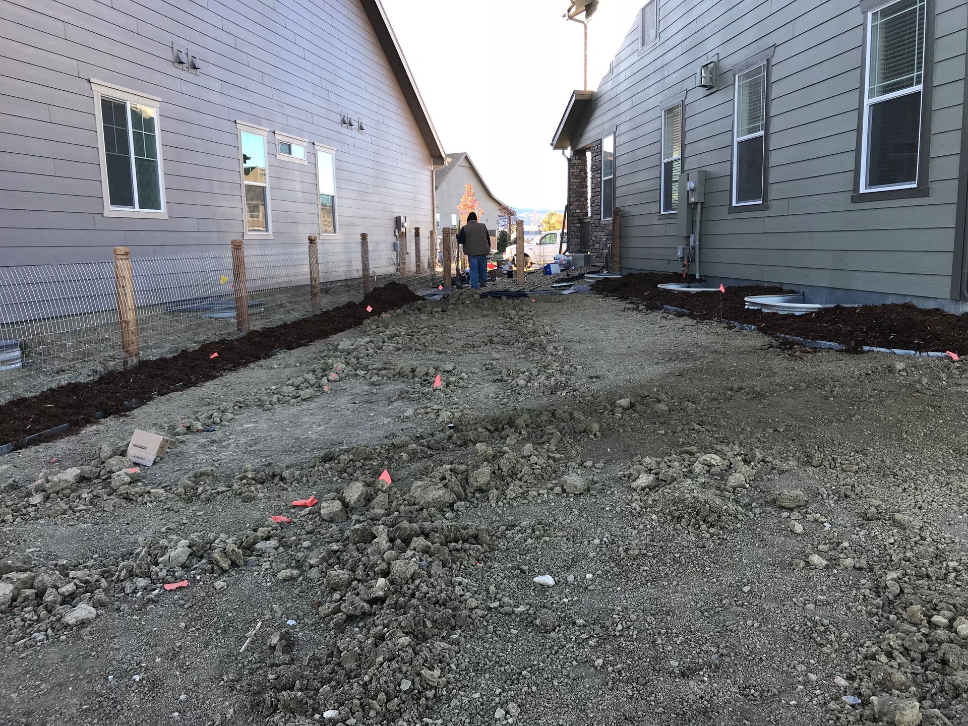 Gravel pathway between two gray houses under construction; workers in the distance.
