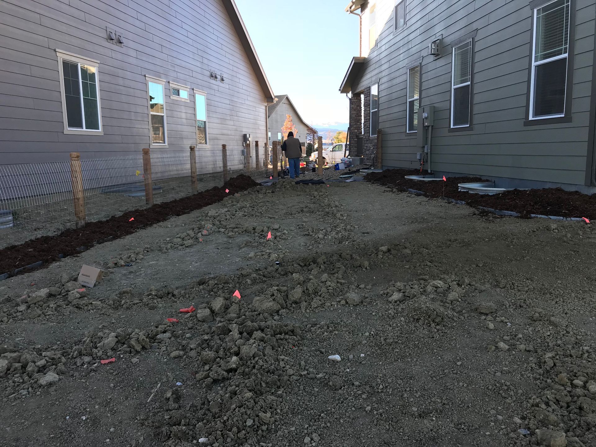 Construction site with two houses. A gravel path and workers in the distance.