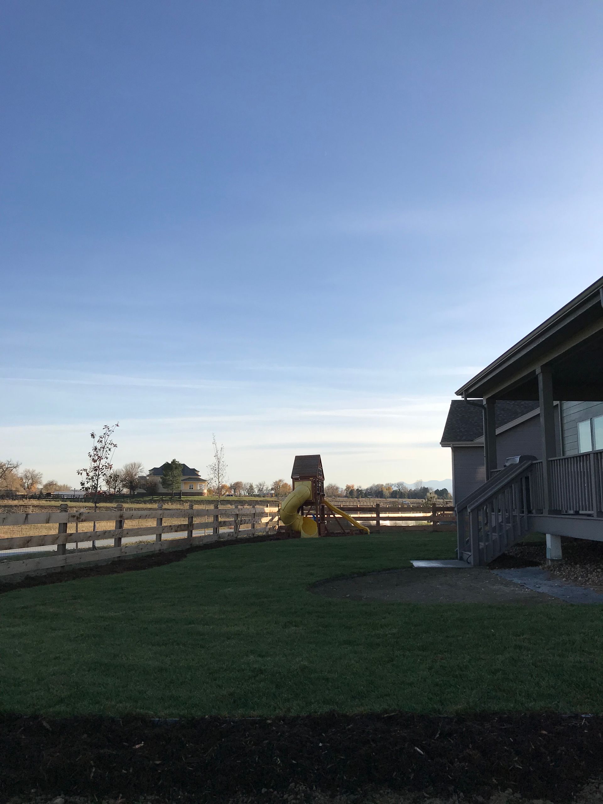 A backyard with a wooden fence, slide, and house under a blue sky.