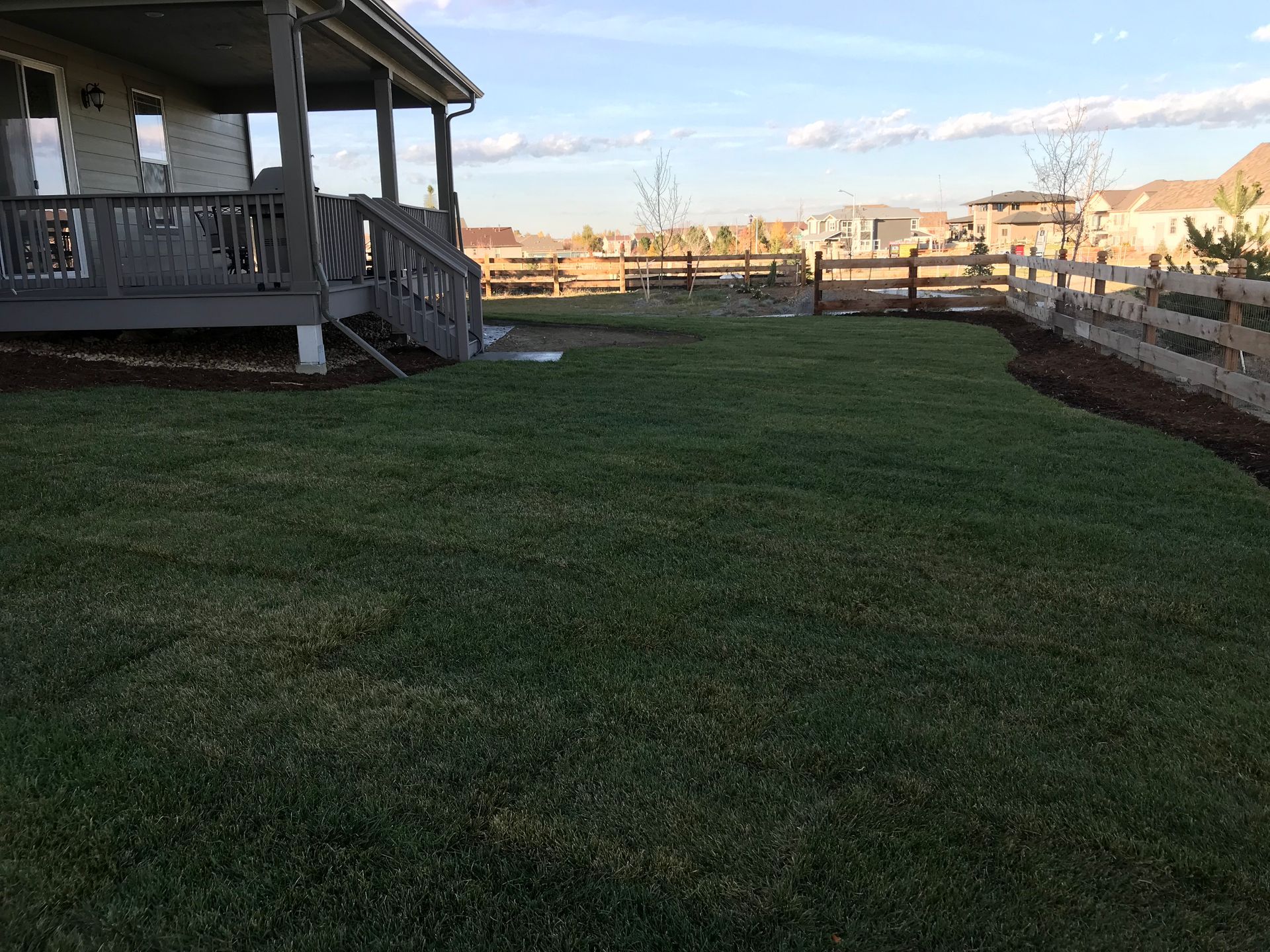 Green lawn backs up to a wooden fence and house with a porch in a suburban setting.
