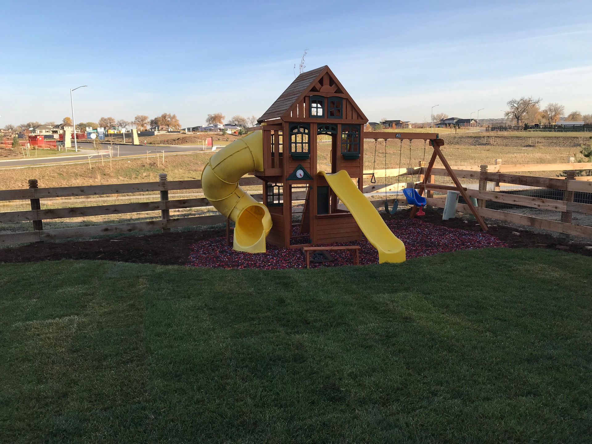 Wooden playset with yellow slides and swing set on green grass.