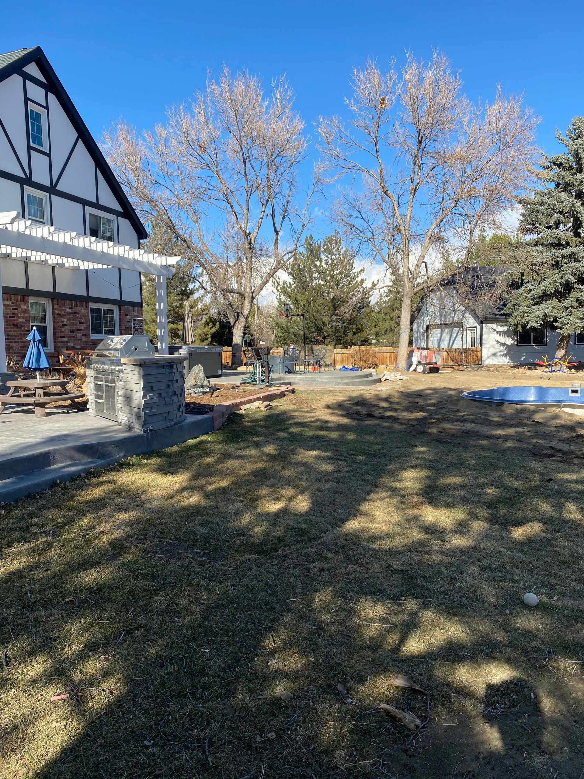 Backyard with a house, trees, patio, and sunny sky.