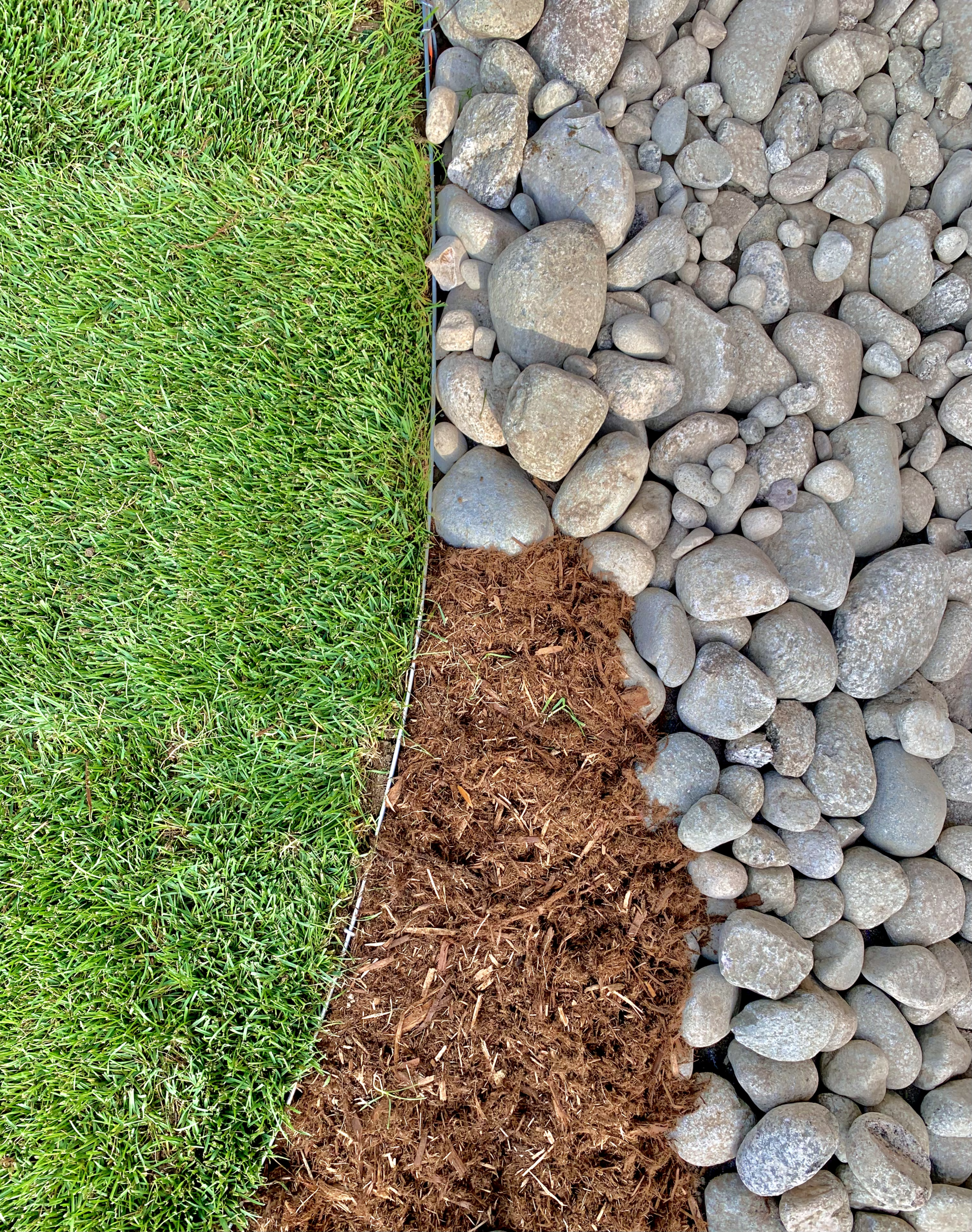 Green grass, brown mulch, and gray river rock border a yard.