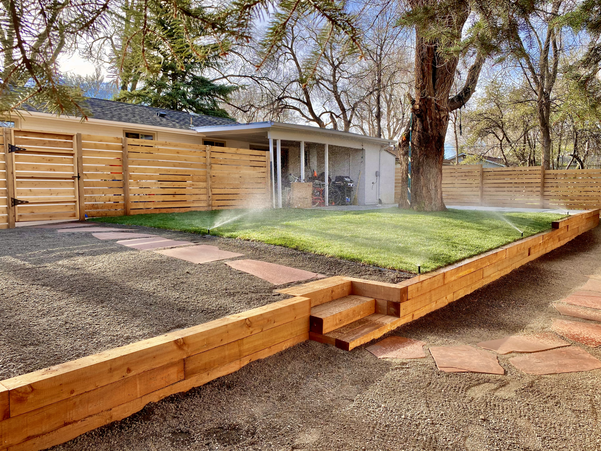 Wooden raised bed with steps, grassy area, and wooden fence around a house.