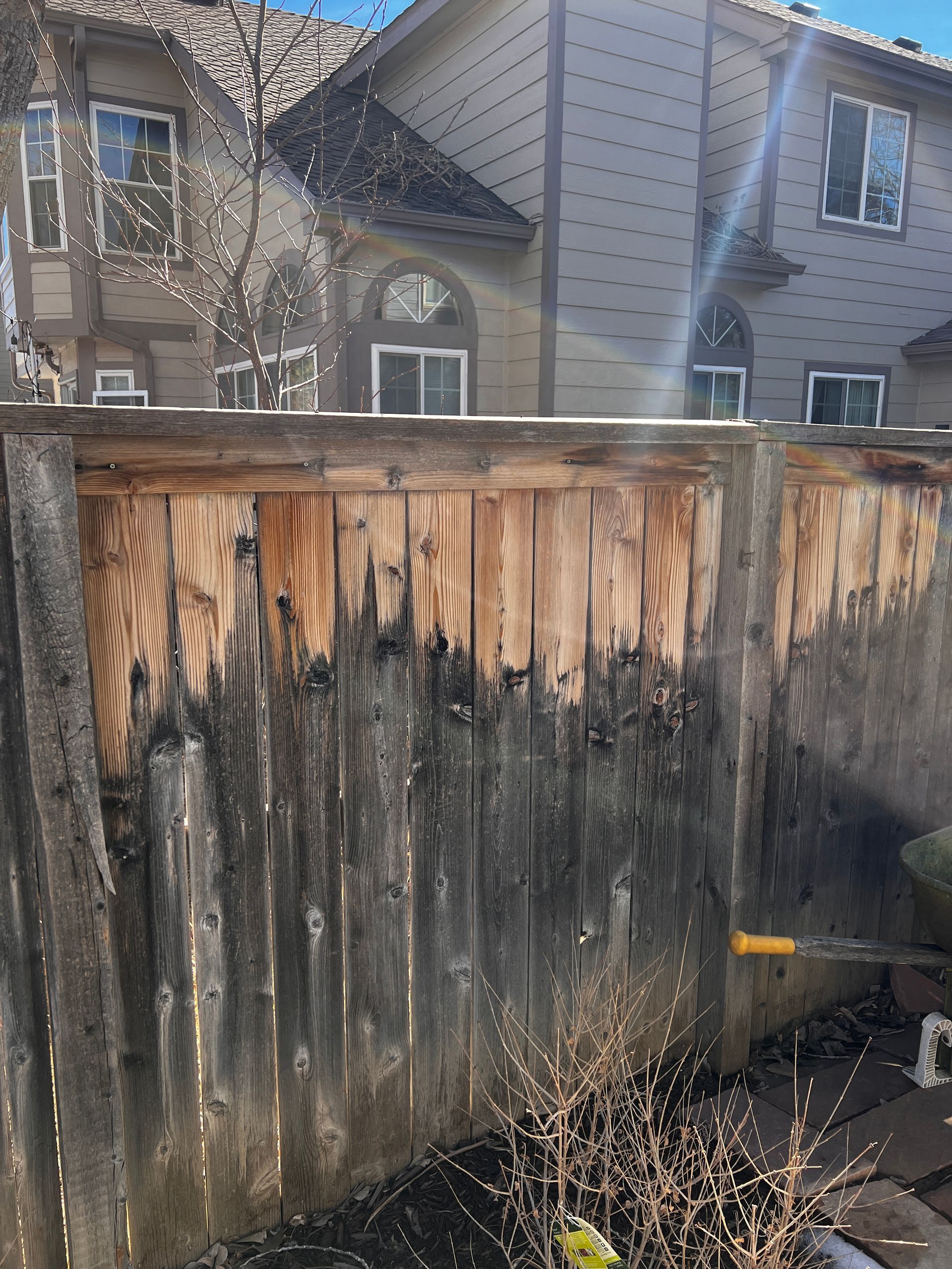 Fence with dark discoloration, partially cleaned, house in the background.