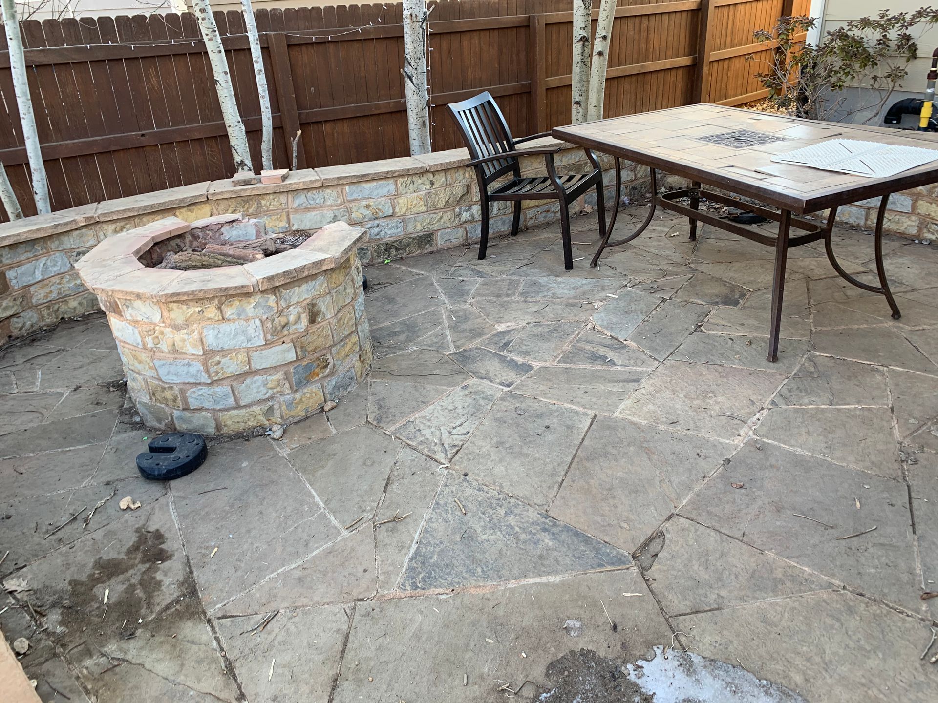 Patio with fire pit, table, and chair. Brown stone wall and flagstone floor.