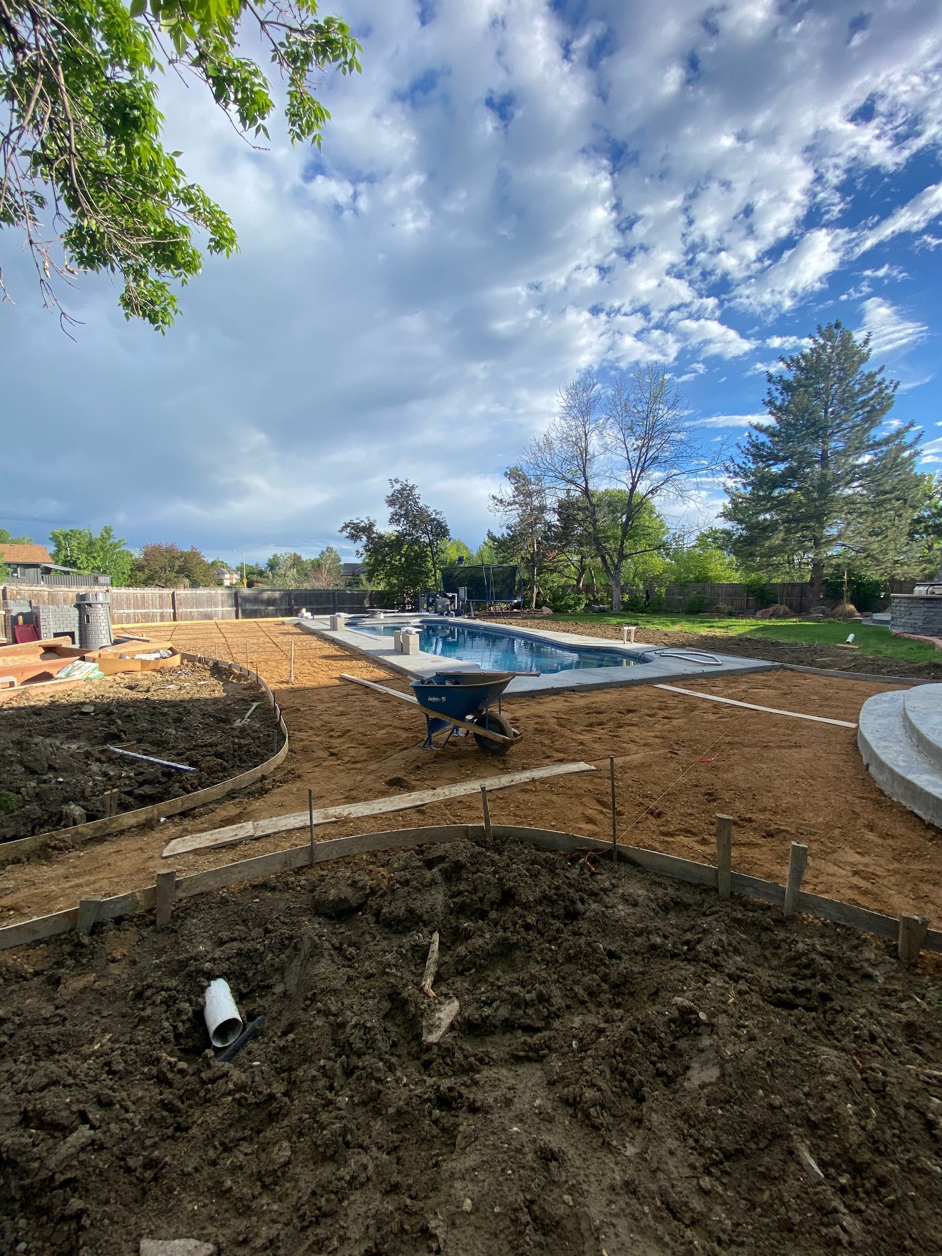 Backyard under construction with a pool, dirt, and cloudy sky.