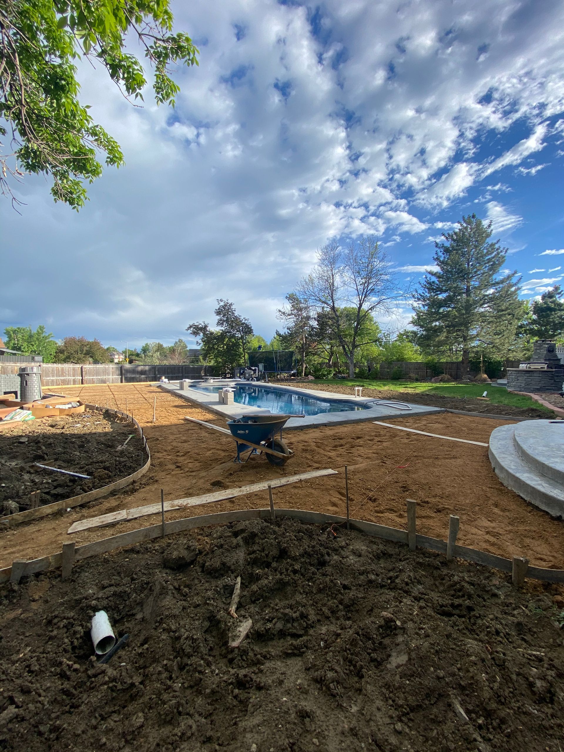 Backyard under construction with a pool, pathways, and dirt under a cloudy sky.