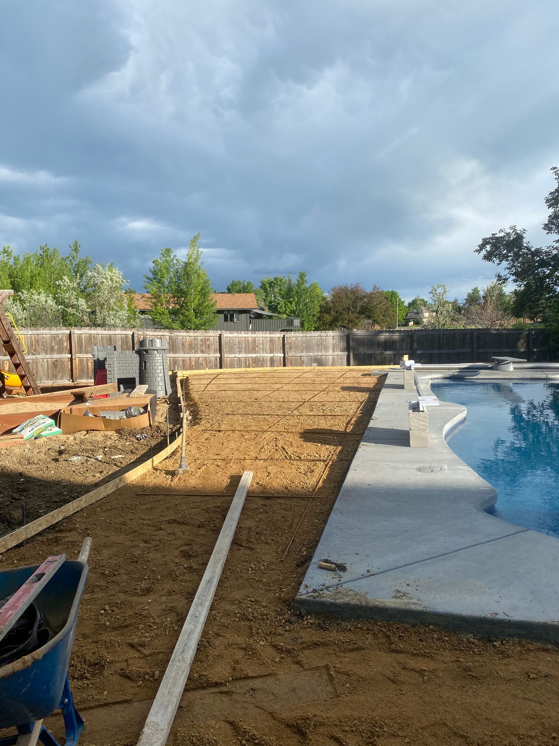 Backyard with construction: Dirt area next to a pool being prepared for a project; cloudy sky overhead.