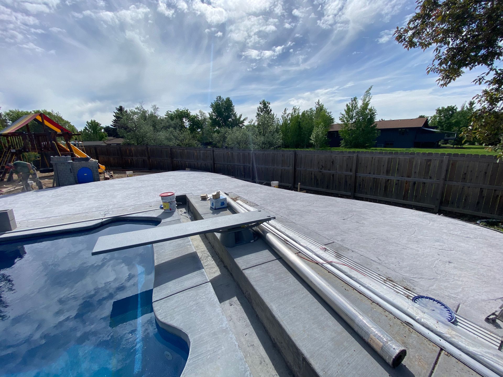 Backyard with pool, diving board, and gravel area; cloudy sky overhead.