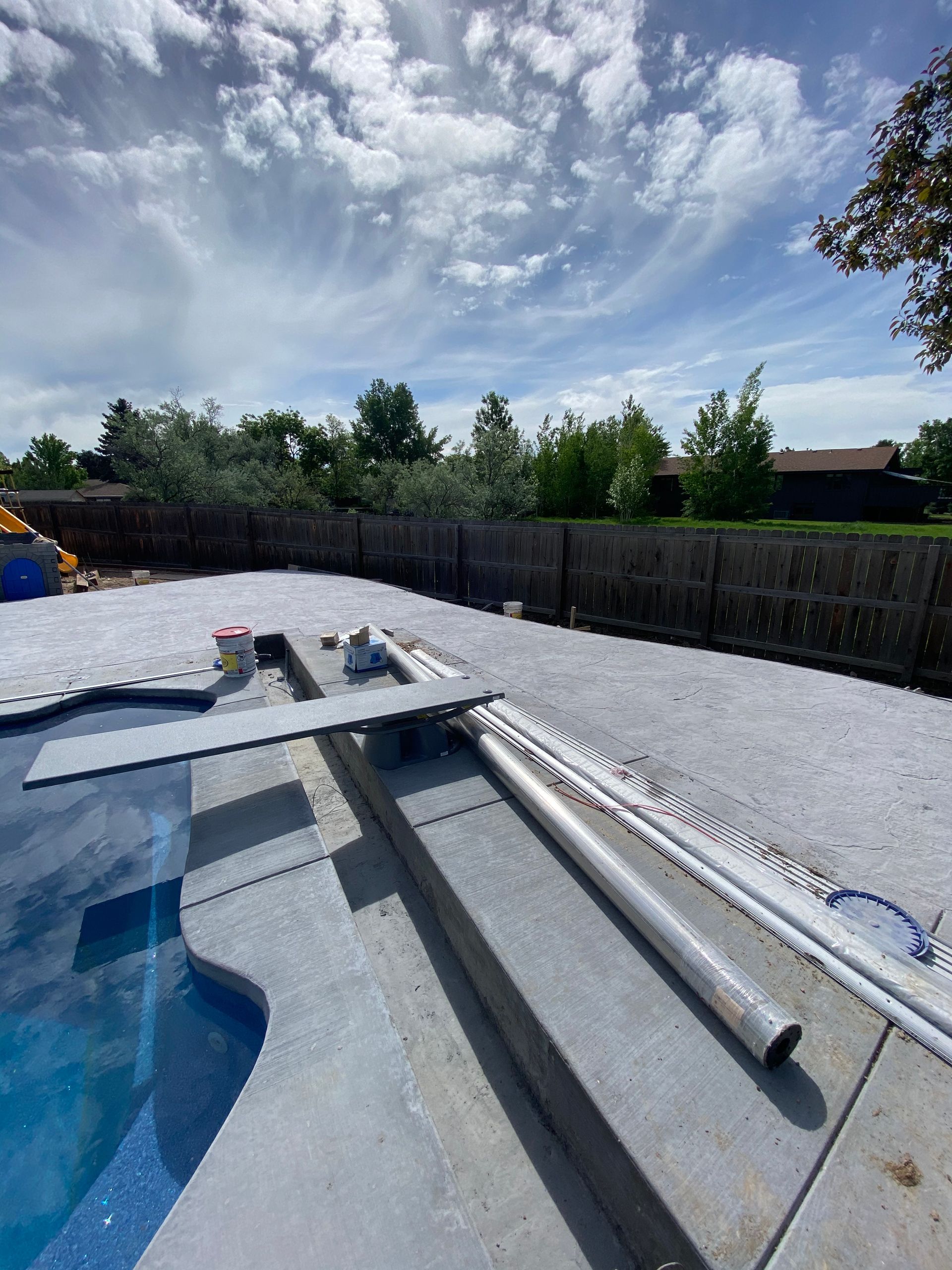 Pool with open cover, concrete deck, blue water, and cloudy sky.