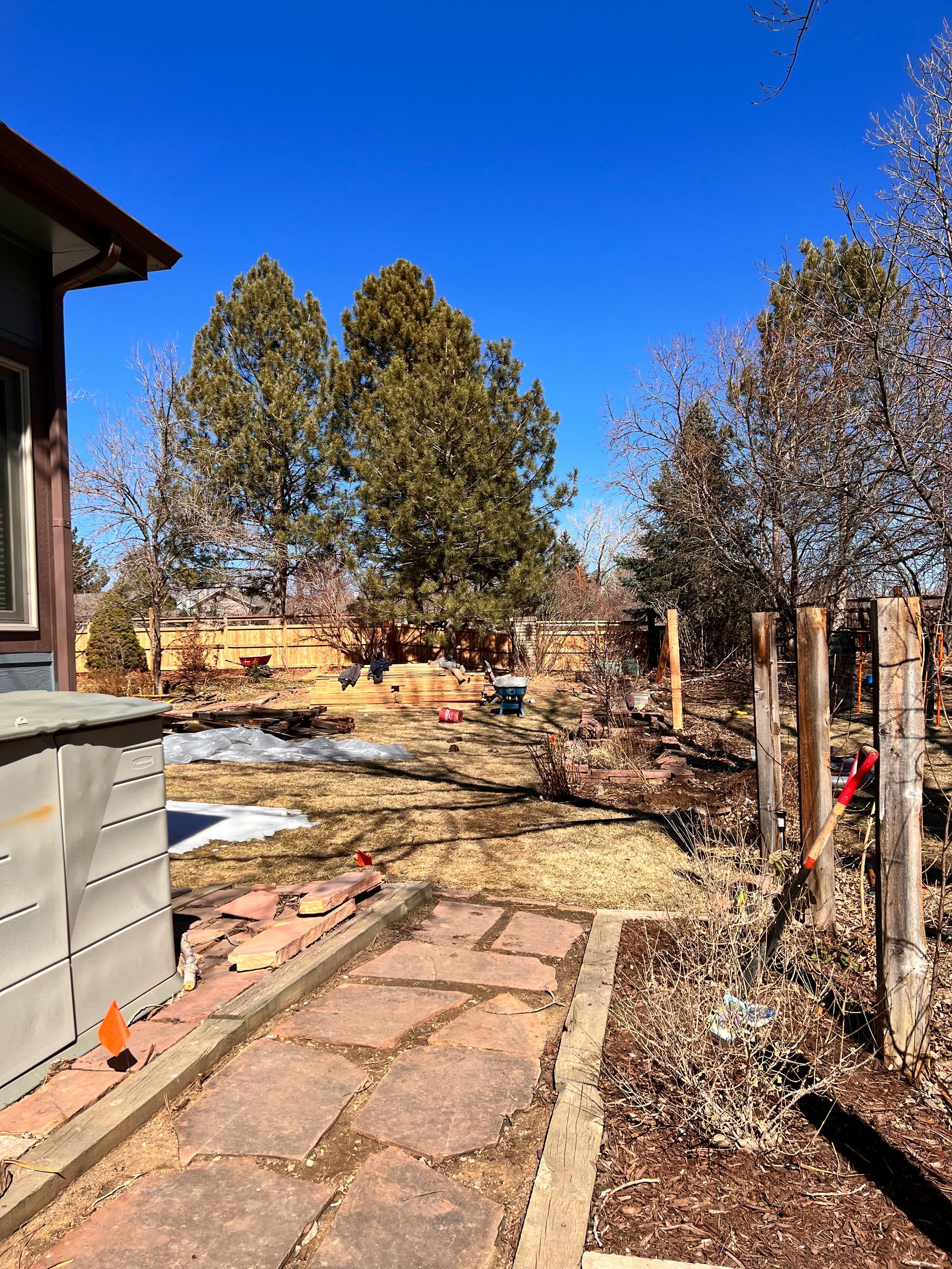 Stone path leads through a yard with a house, trees, and fence on a clear, sunny day.