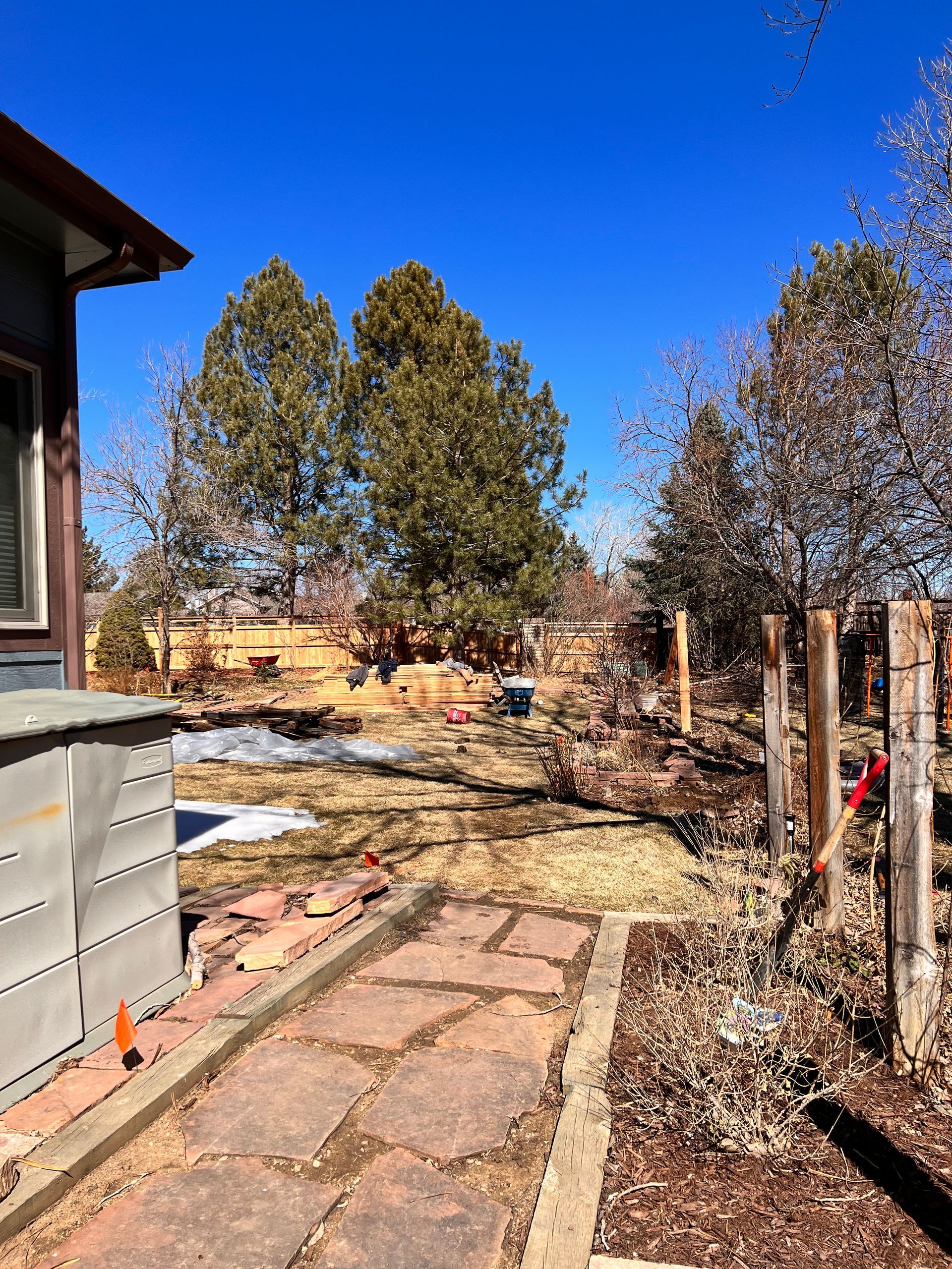 Backyard with stone path, shed, fence, trees, and blue sky.