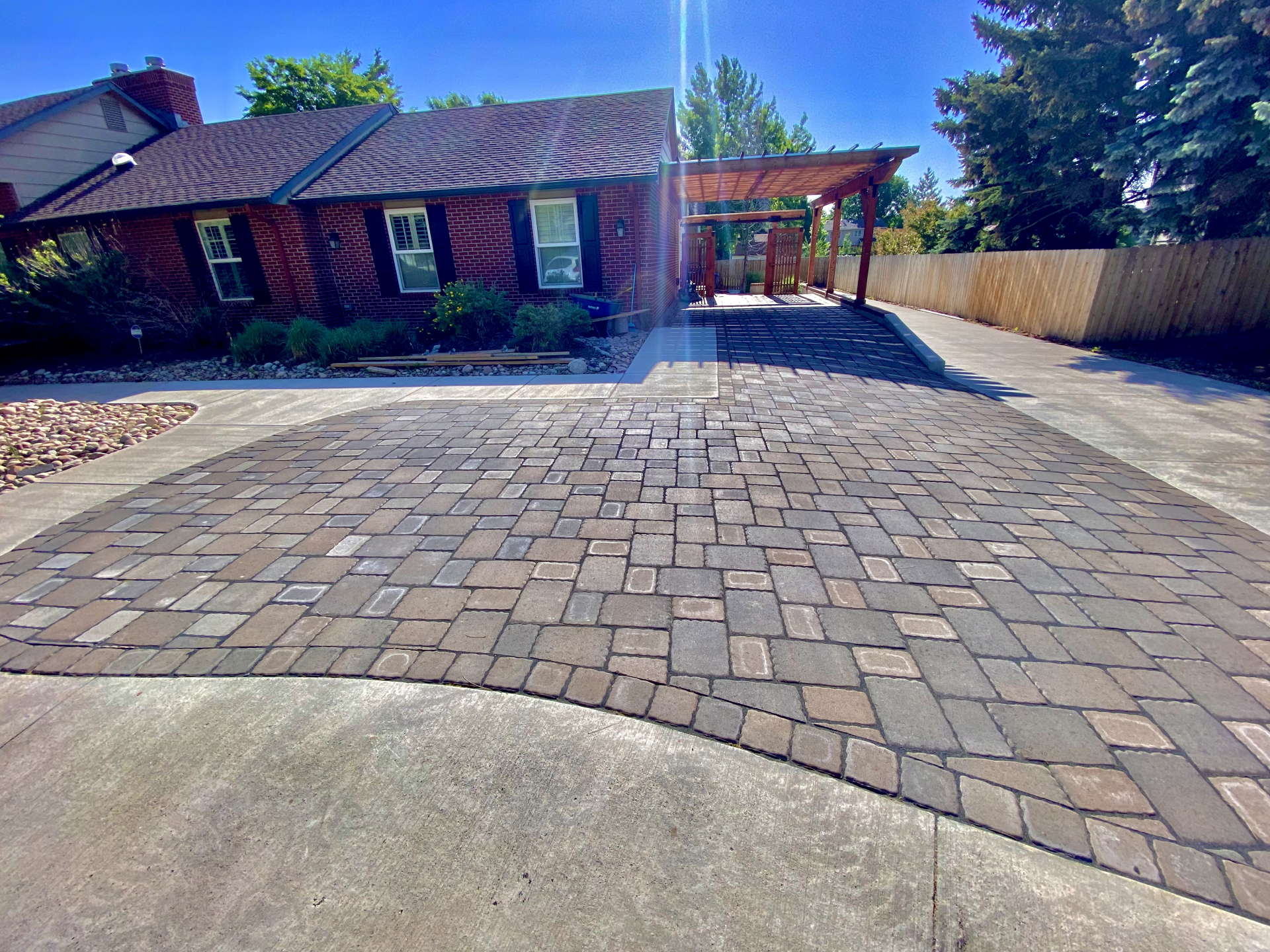 Brick paver driveway leading to a brick home with a pergola on a sunny day.