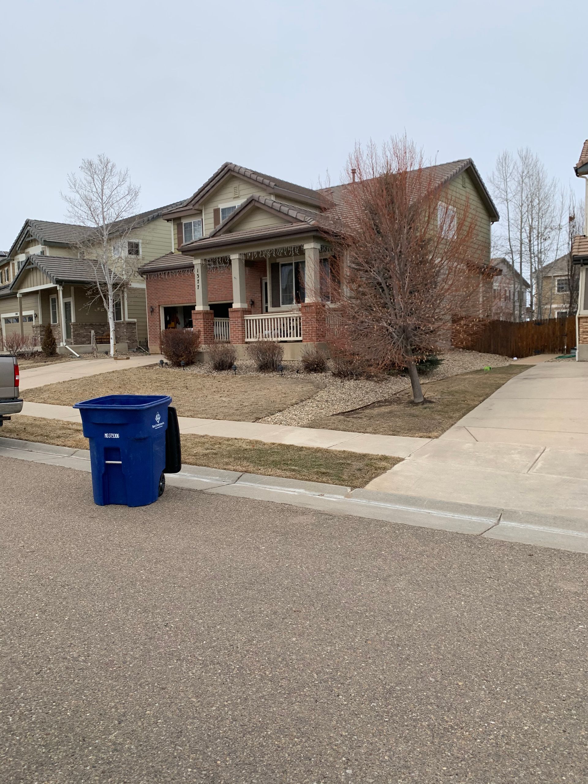 House with red brick and porch, blue trash bin in front.