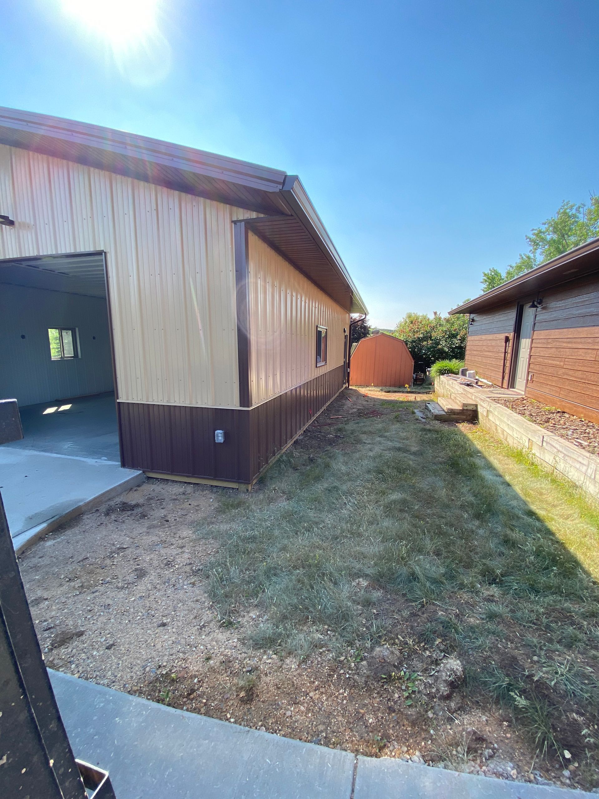 A tan and brown building with an open garage door, green grass, and another brick building on the right.