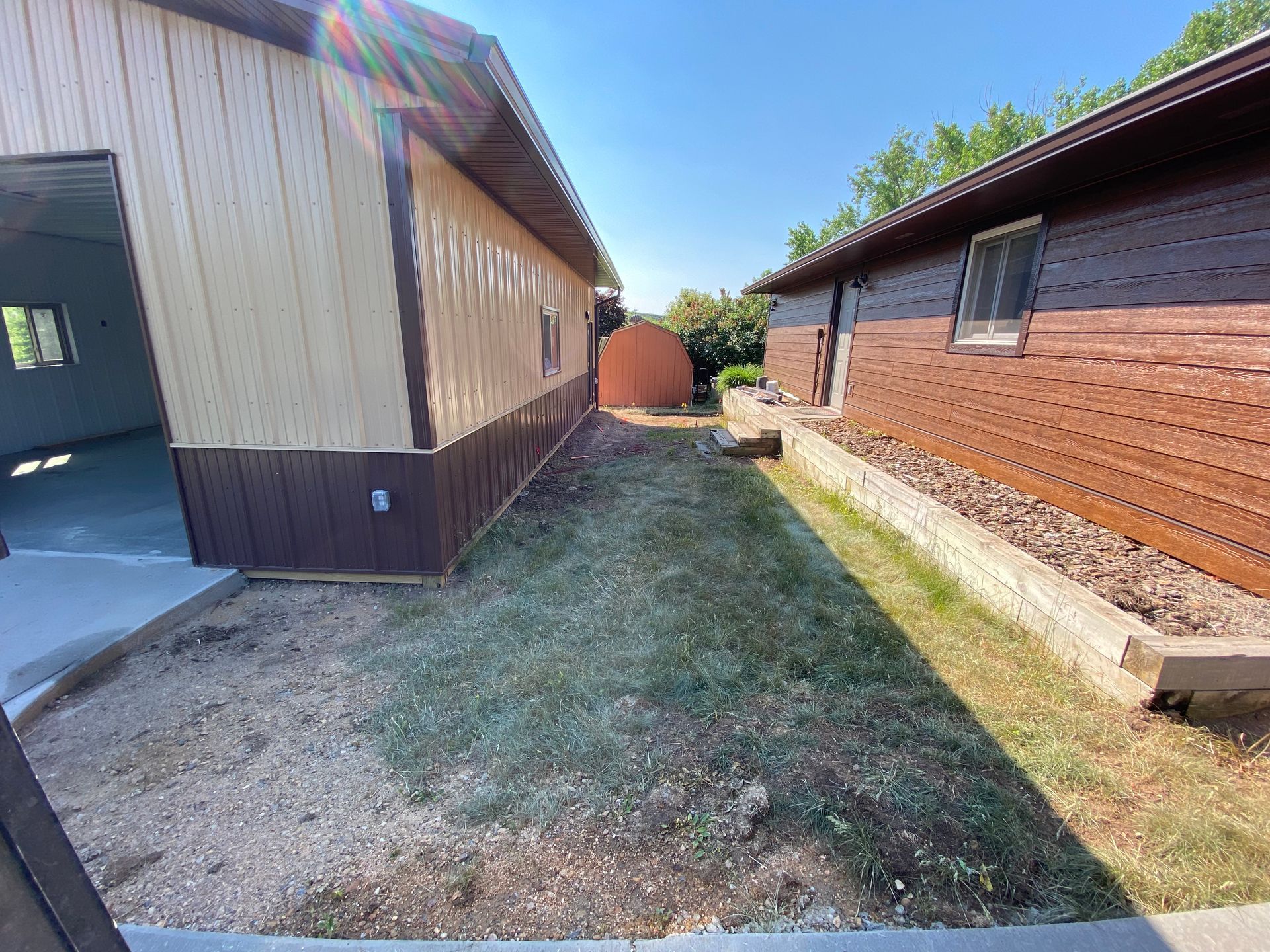 A narrow yard between two buildings, one tan, one brown.