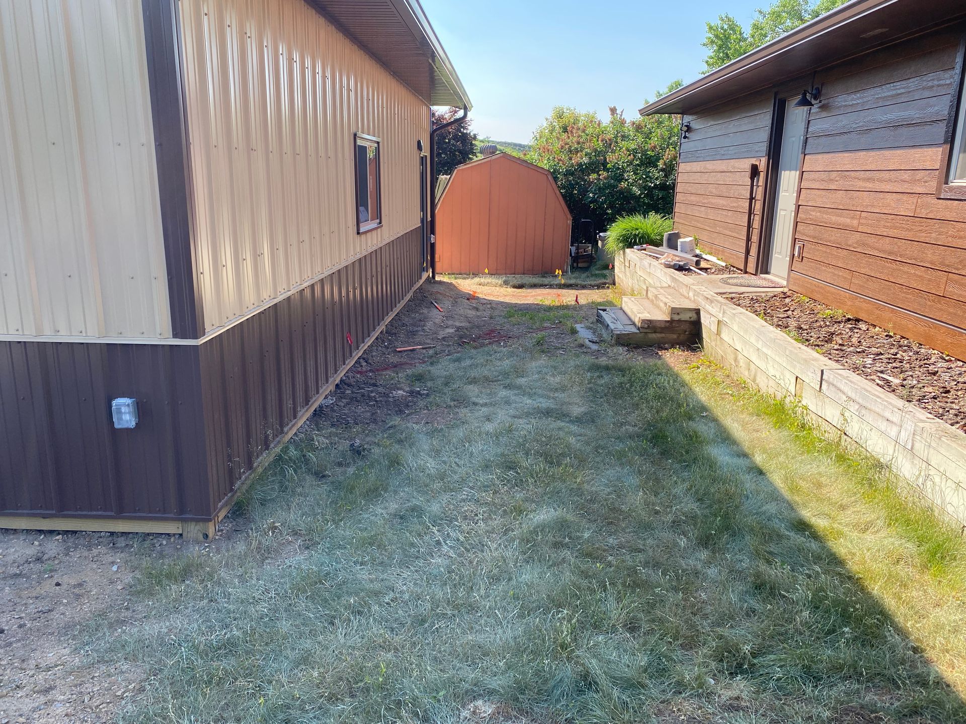 A narrow, grassy yard between two buildings, one tan and brown, the other brick-red.