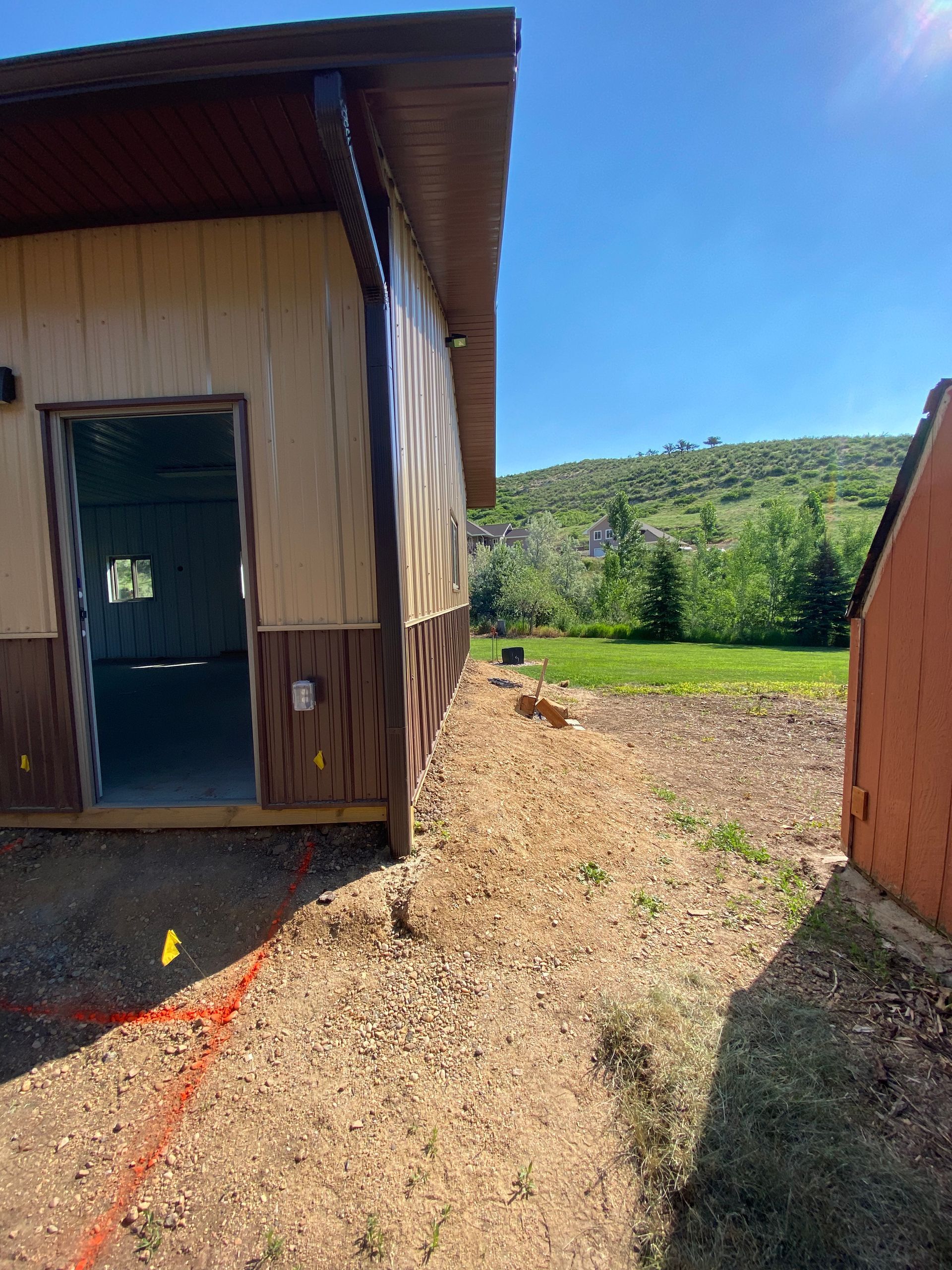 Building exterior with open doorway, gravel path, and grassy hill in the background. Sunny day.