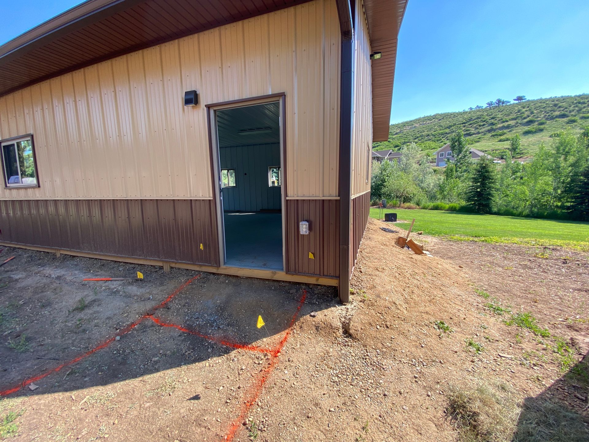 Exterior of a building with a brown and tan facade, doorway open, on a grassy hill, marked with orange lines.
