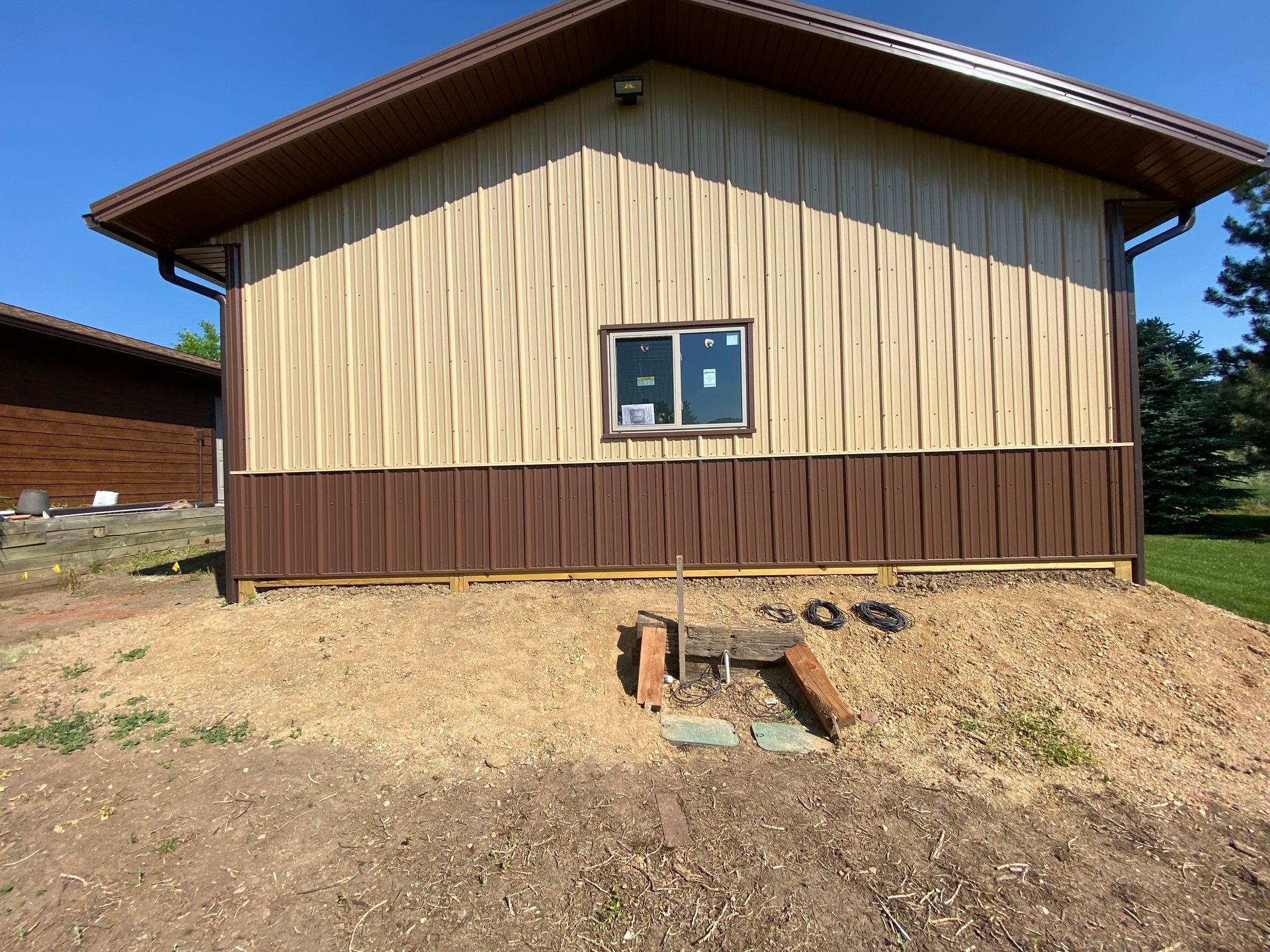 Tan and brown building with a single window, on a gravel base.