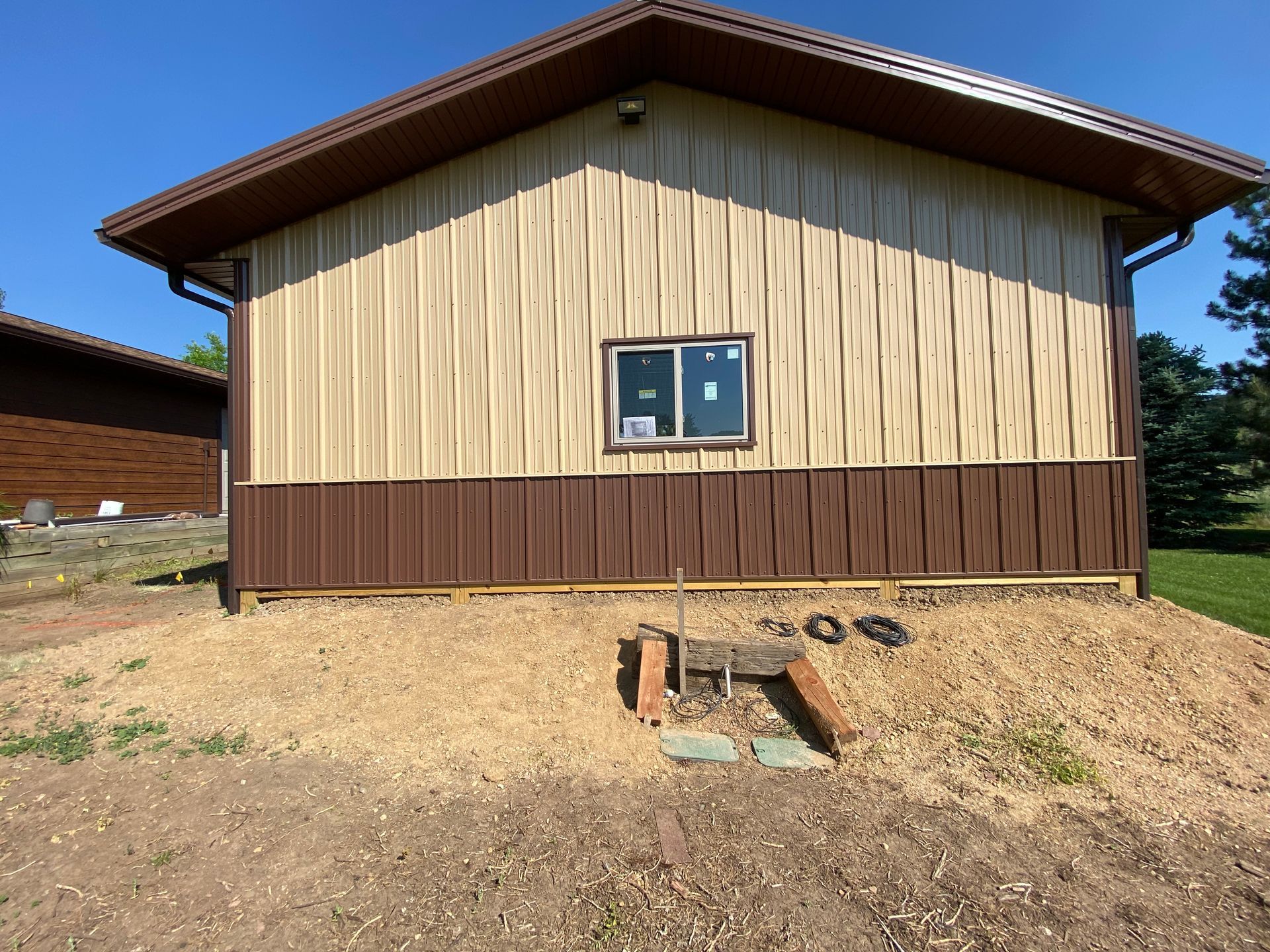 Tan and brown building with a small window, set on gravel ground.