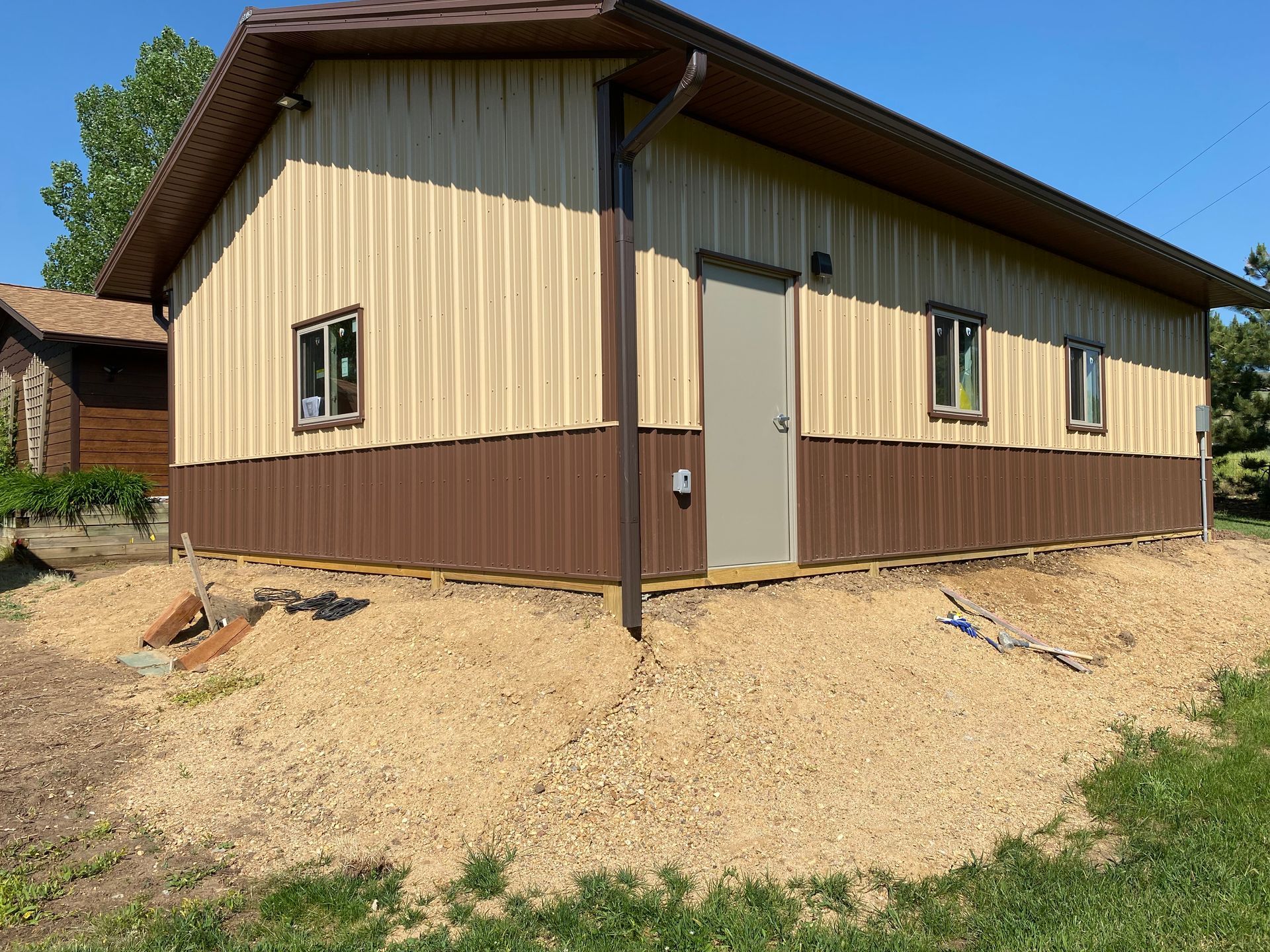 Tan and brown metal building with gravel base and door.