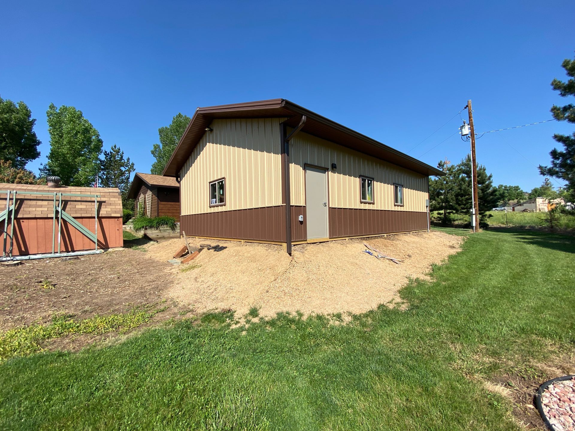 Tan and brown building with a brown roof and a gravel base, set against a blue sky.