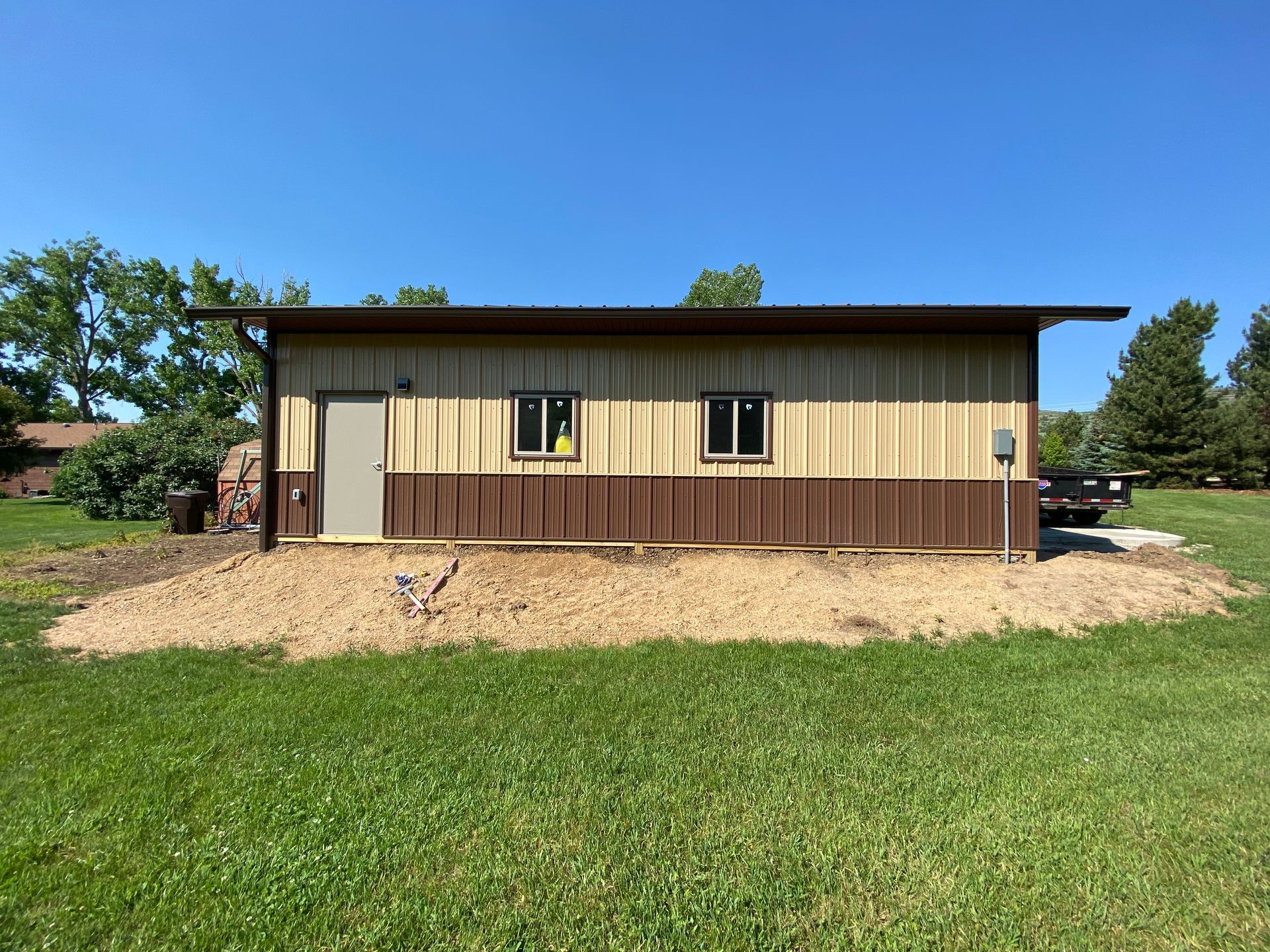 Tan and brown building with a door, two windows, and gravel foundation against a clear blue sky.
