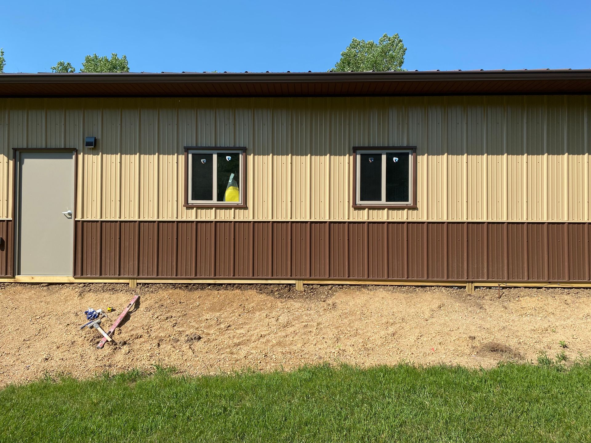 Tan and brown metal building with a door, two windows, and gravel foundation.
