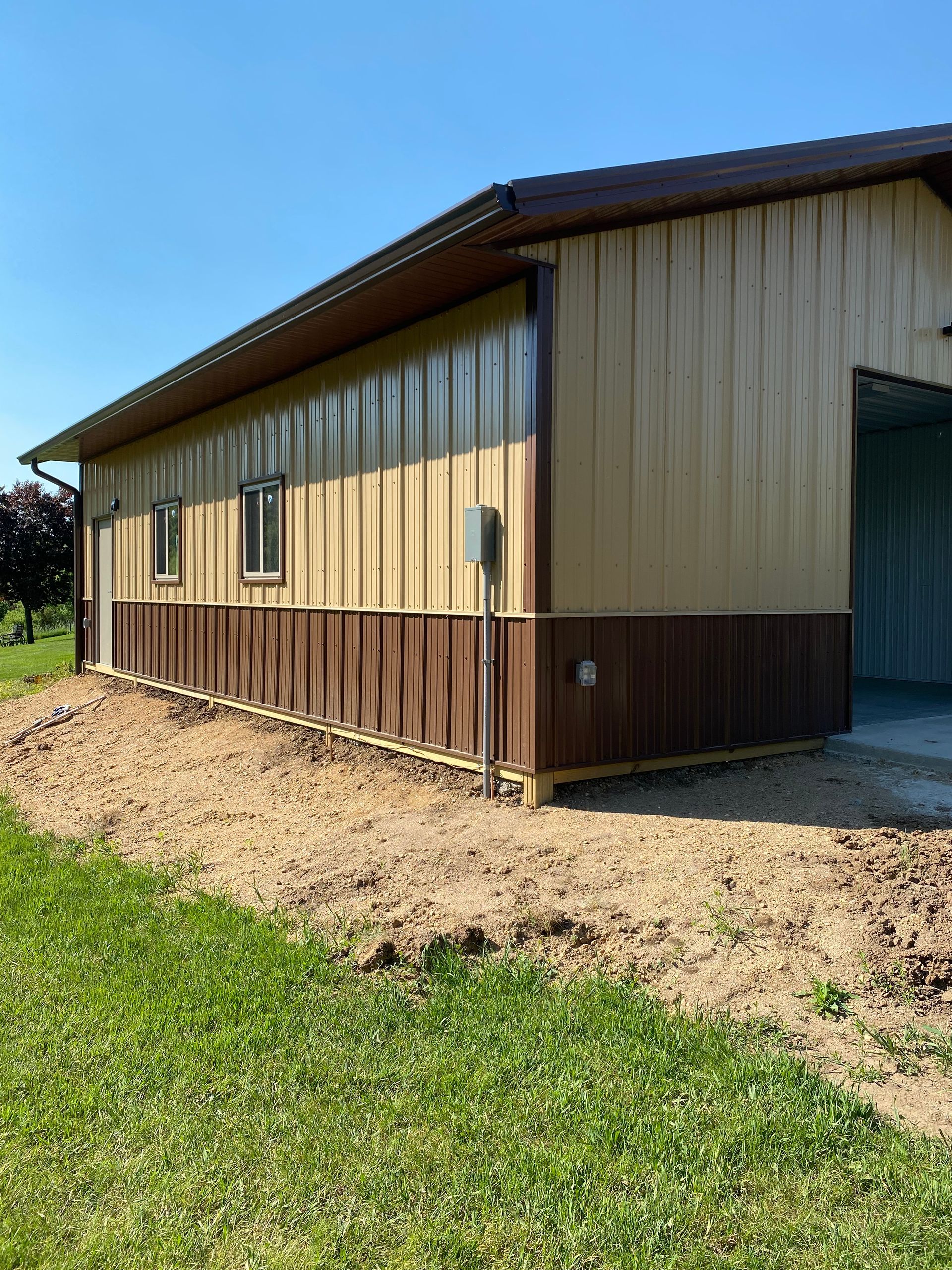 Tan and brown metal-clad building with a dirt path in front, under a blue sky.