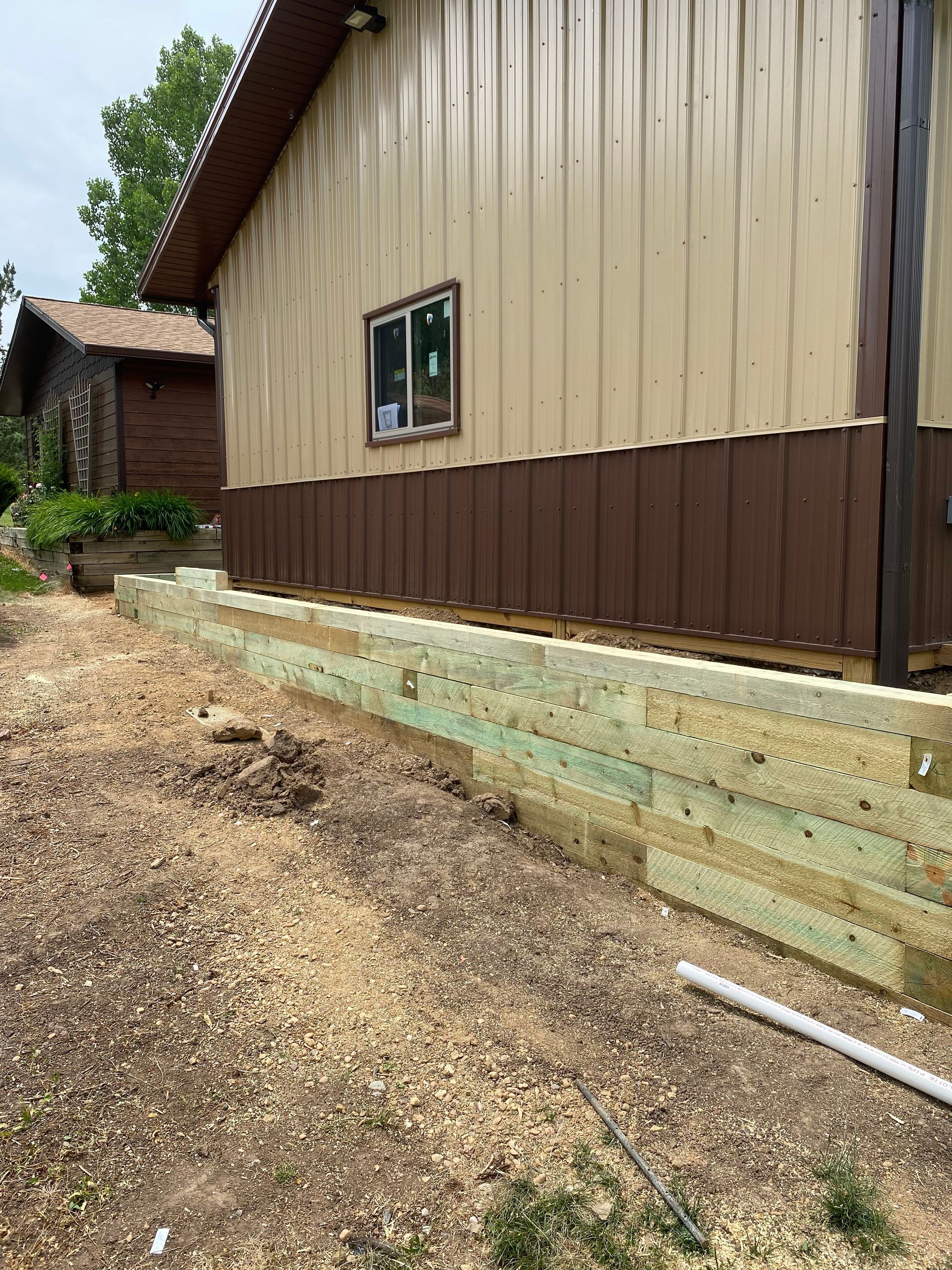 Wooden retaining wall next to a tan and brown building, outdoors.