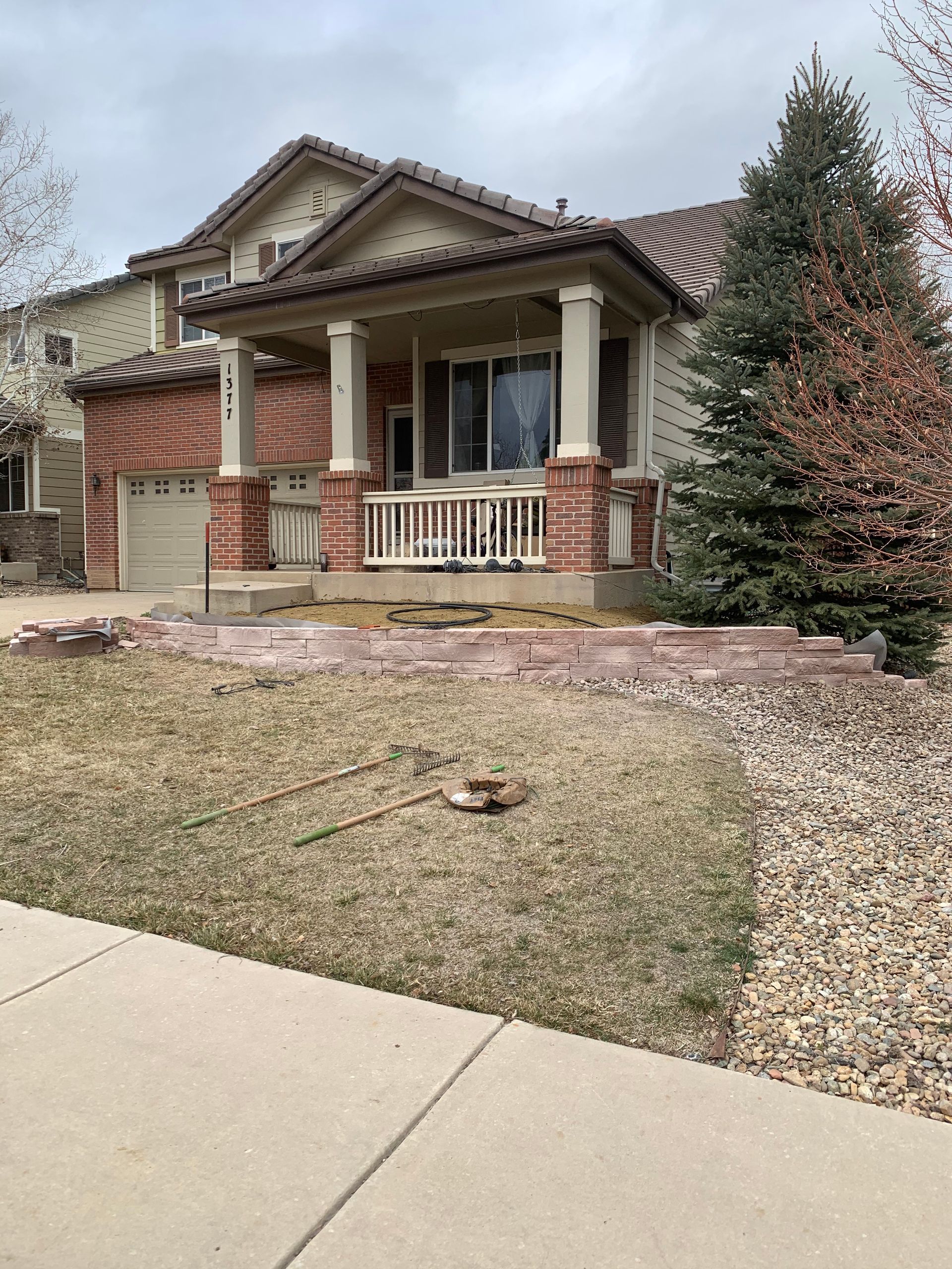Two-story house with a porch and brick accents; front yard has dry grass and landscaping.