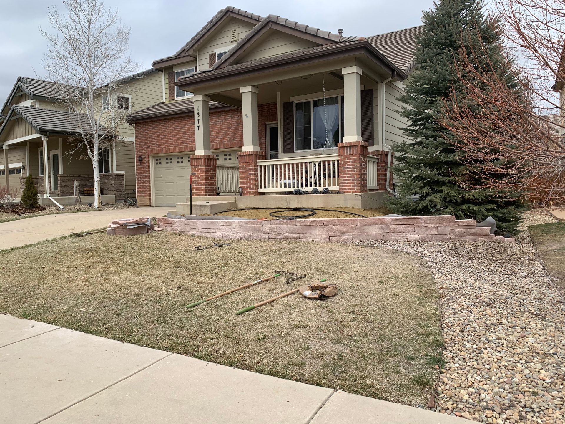 Two-story house with brick accents, porch, and a gray sky. A brown lawn in front with gravel pathway.