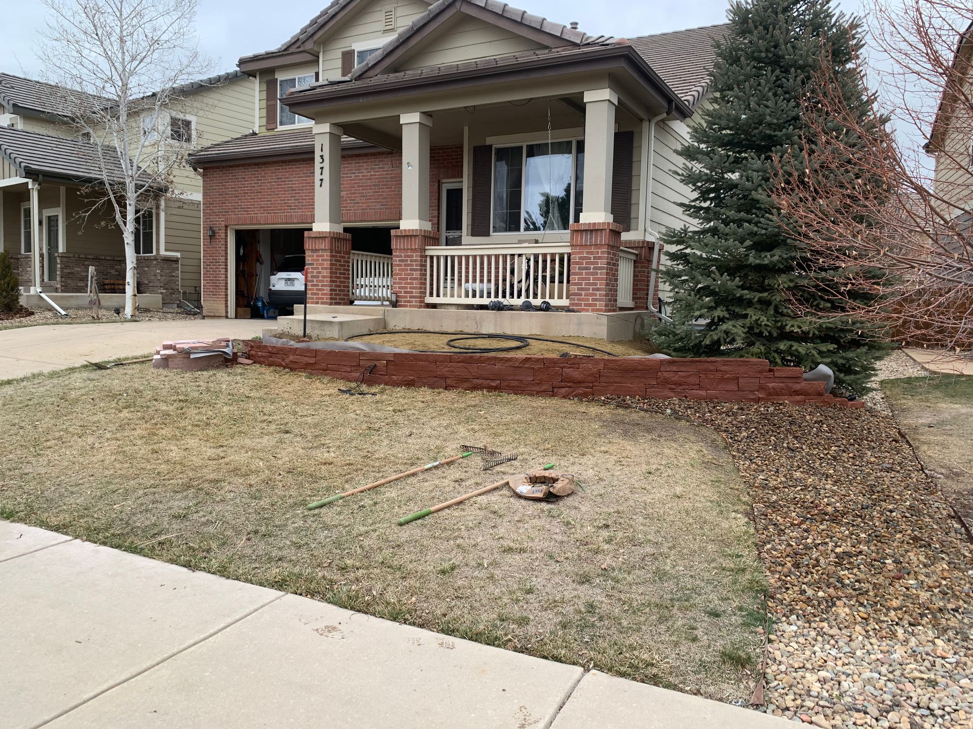 Two-story house with porch, brick accents, and lawn partially covered in brown mulch.