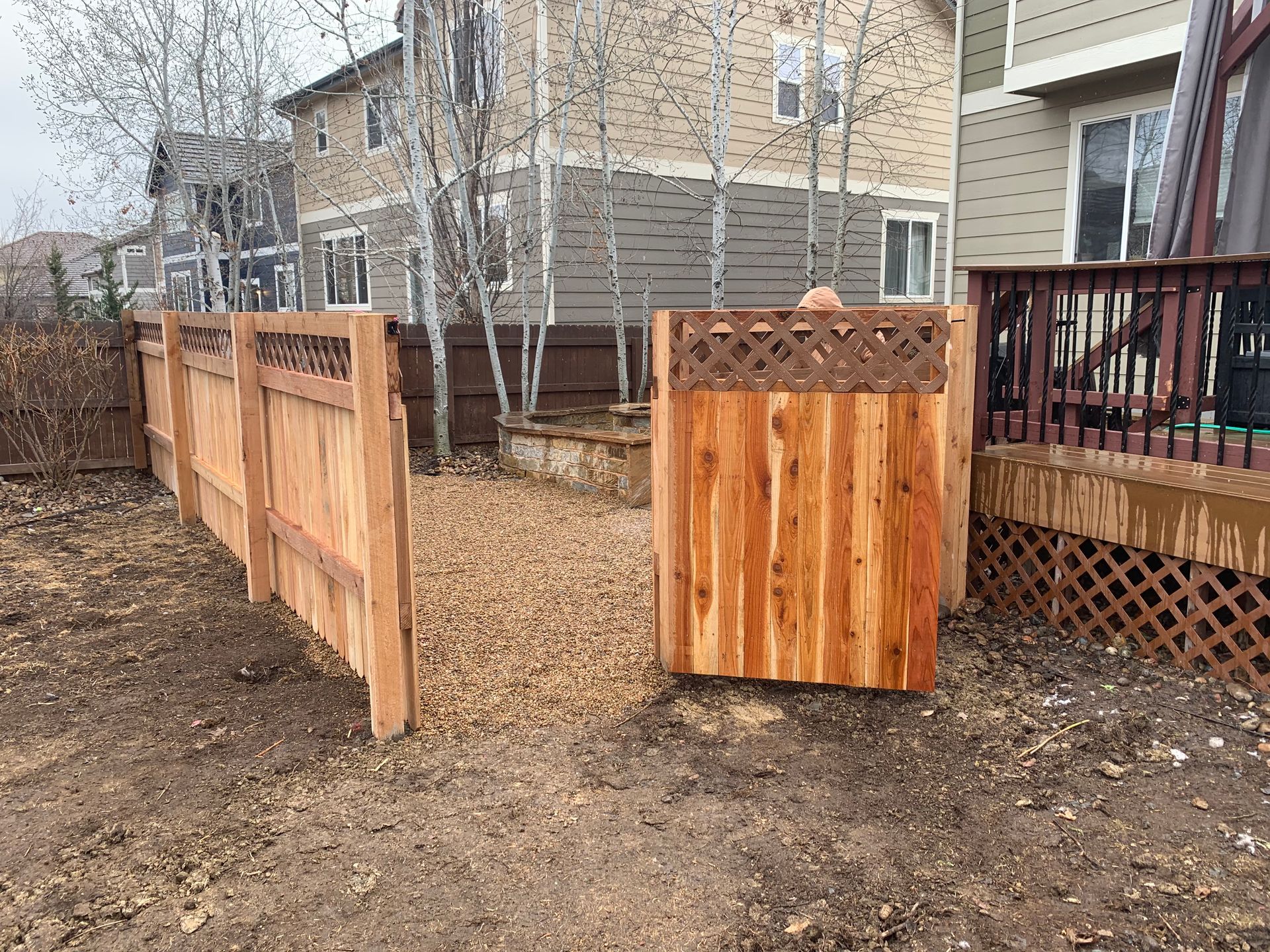 Wooden fence and gate in a backyard with gravel path, and houses in the background.