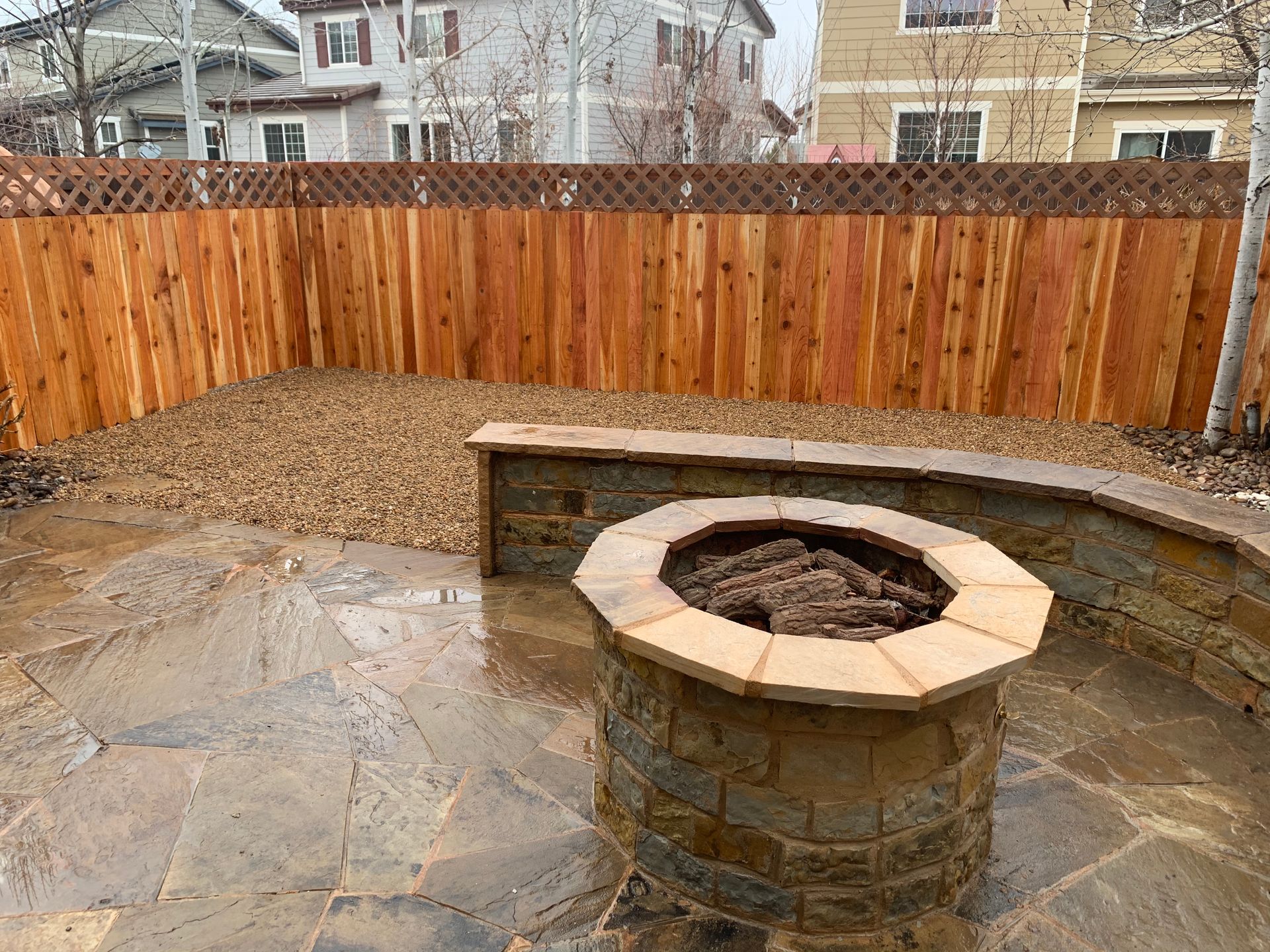 Fire pit on a stone patio with a wood fence and gravel in the background.