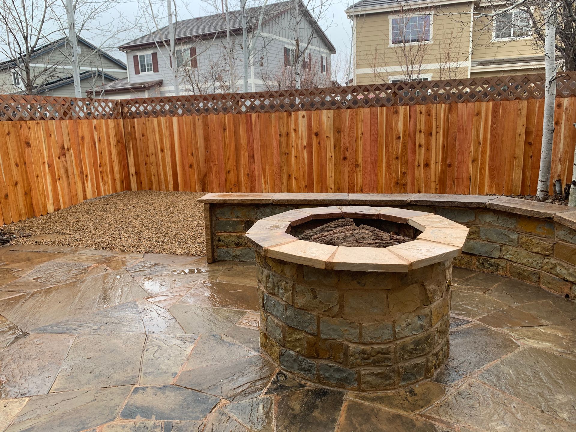 Stone fire pit in backyard with wood fence and landscaping.