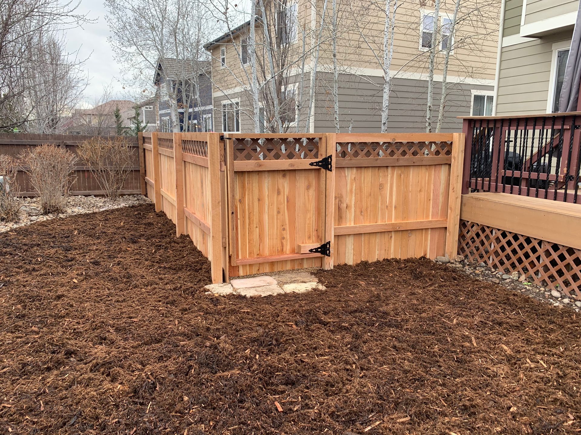 Wooden fence with a gate, in a backyard covered in mulch.