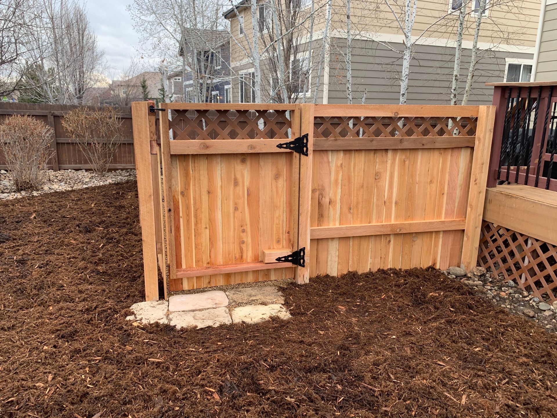 Wooden fence and gate with dark mulch in yard.