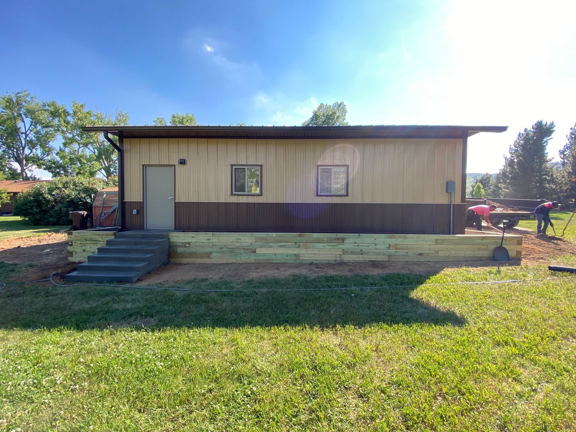Building with brown and tan siding, stairs, and a retaining wall on a grassy lawn.