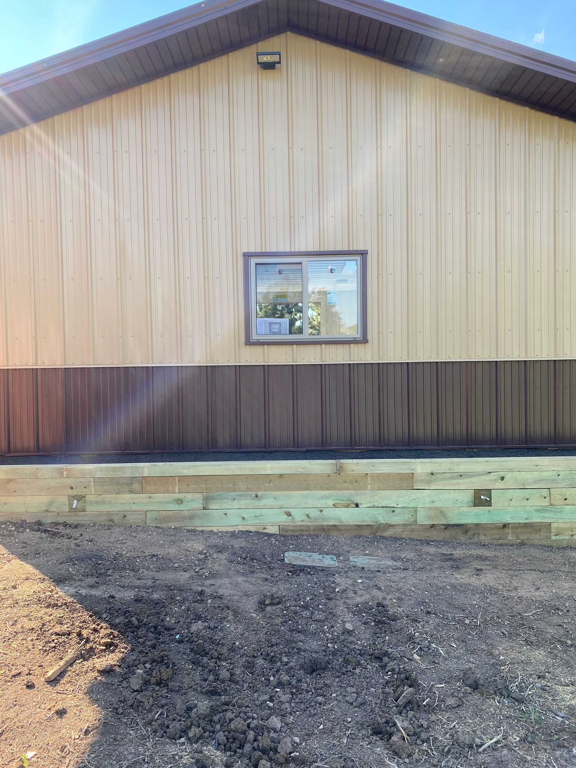 Tan and brown building with a window and a new wooden retaining wall.