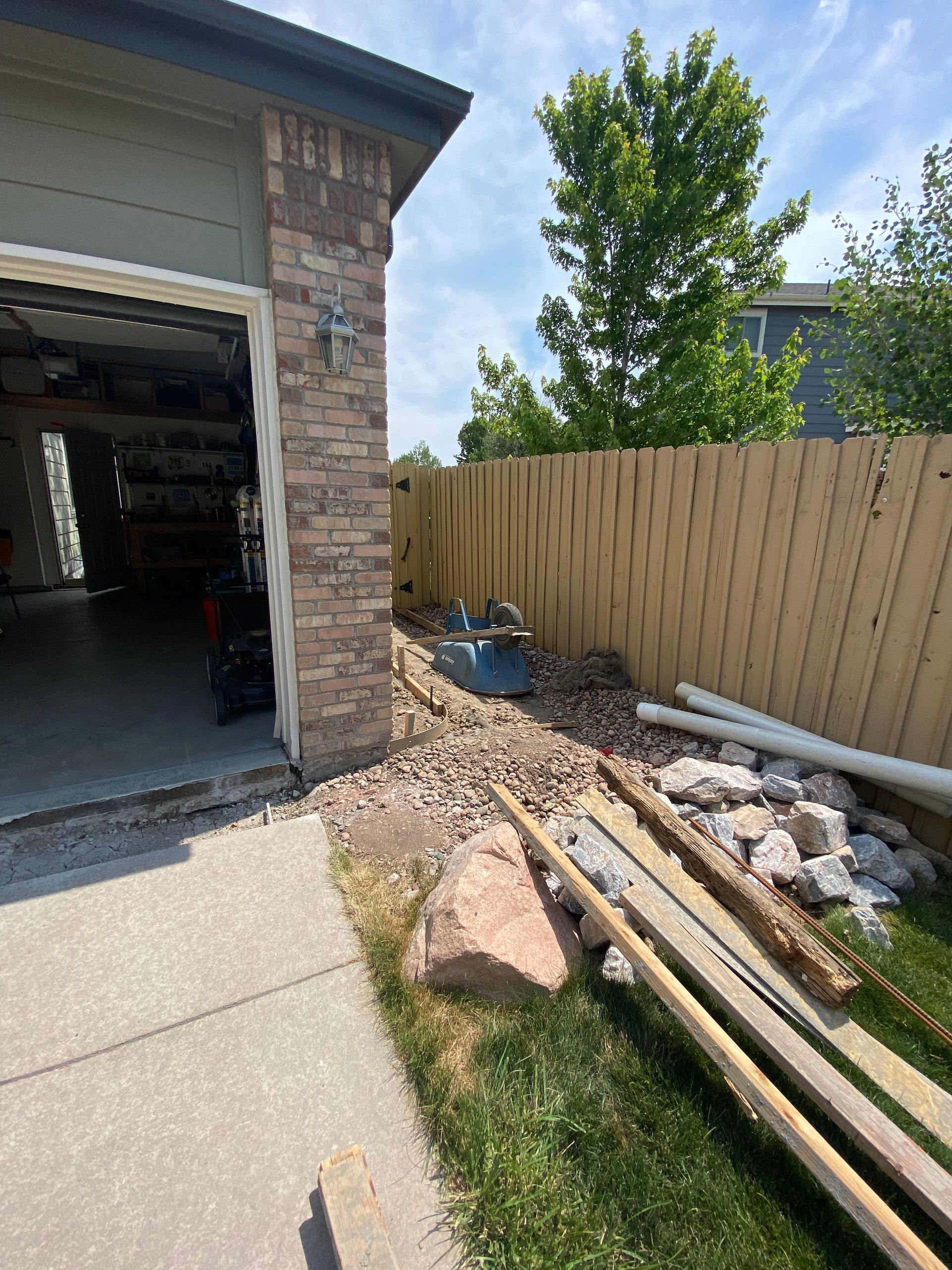 Garage exterior with a brick column and debris on the ground near a wooden fence and lawn.
