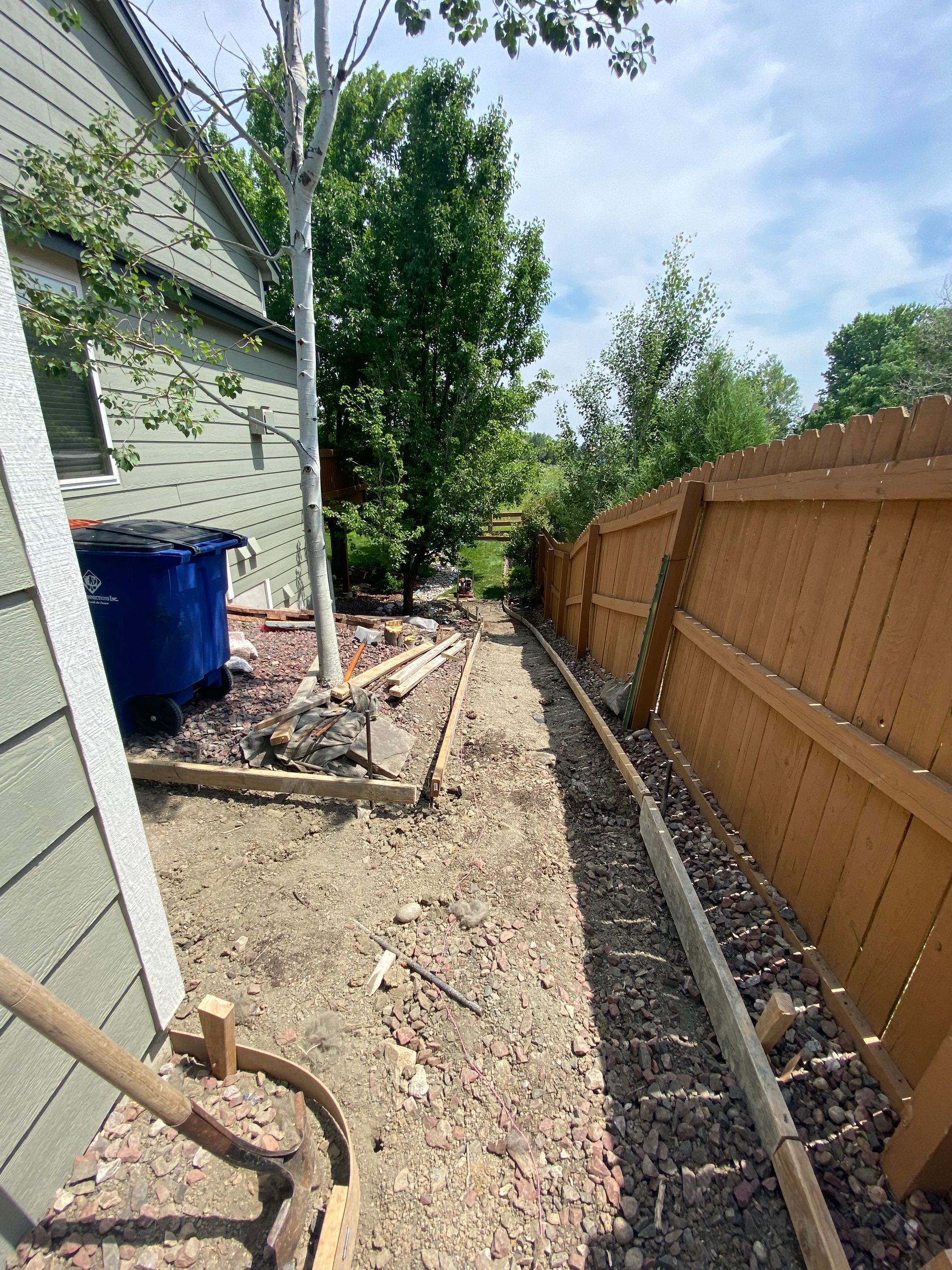 Narrow gravel path between a wooden fence and a house, construction materials visible.