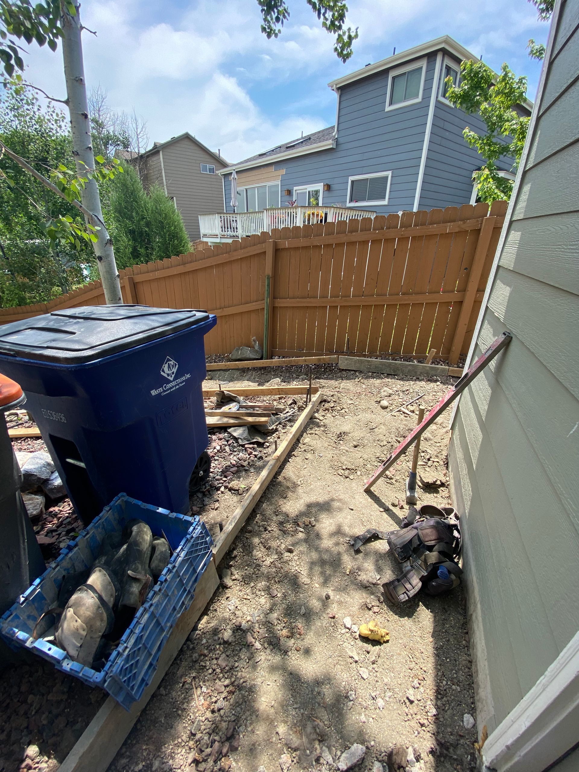 Backyard with trash can, rocks, and wooden fence. Construction materials are visible.