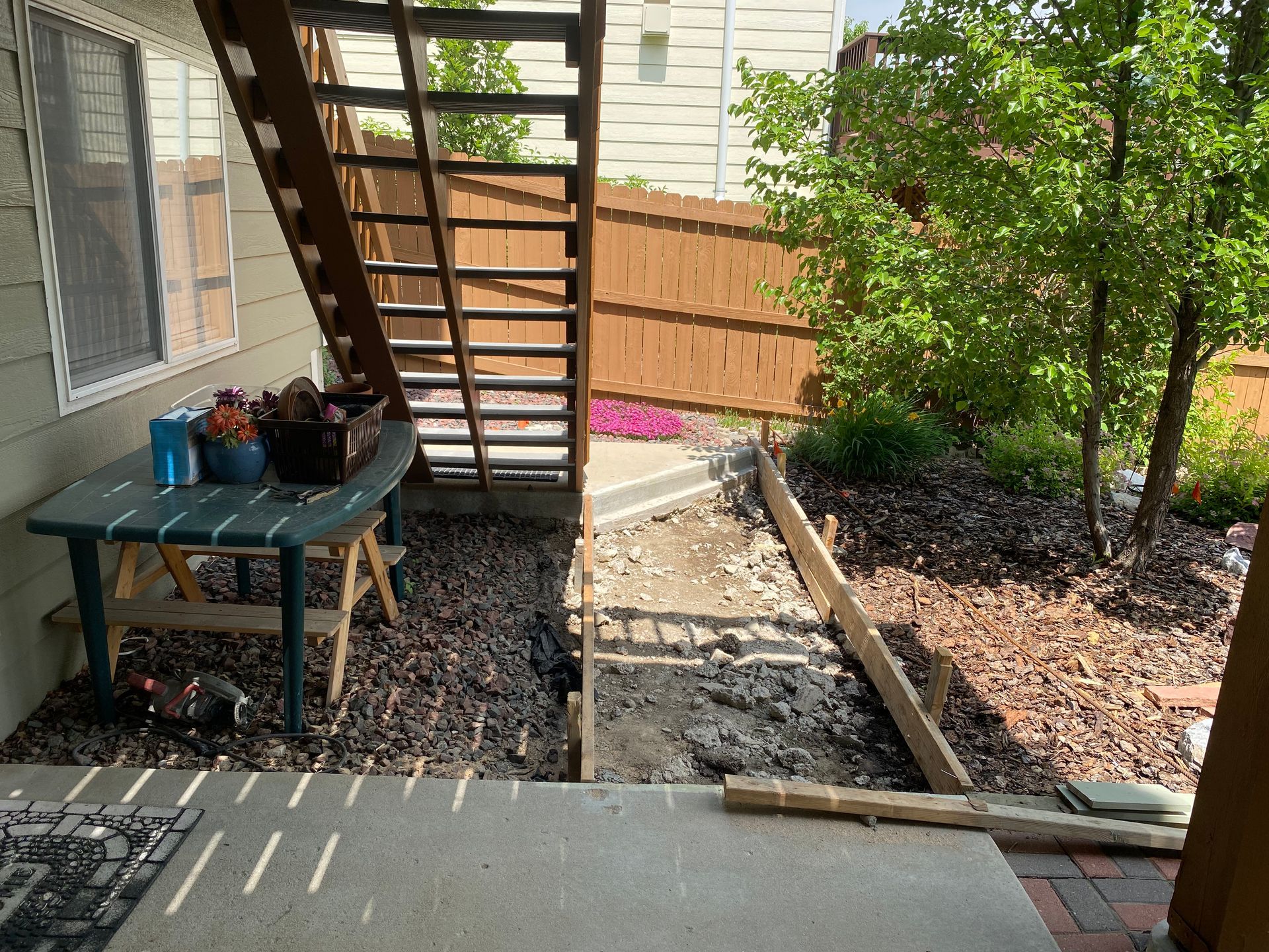 Backyard with stairs, table, and a garden bed under construction, partially paved with brick and concrete.