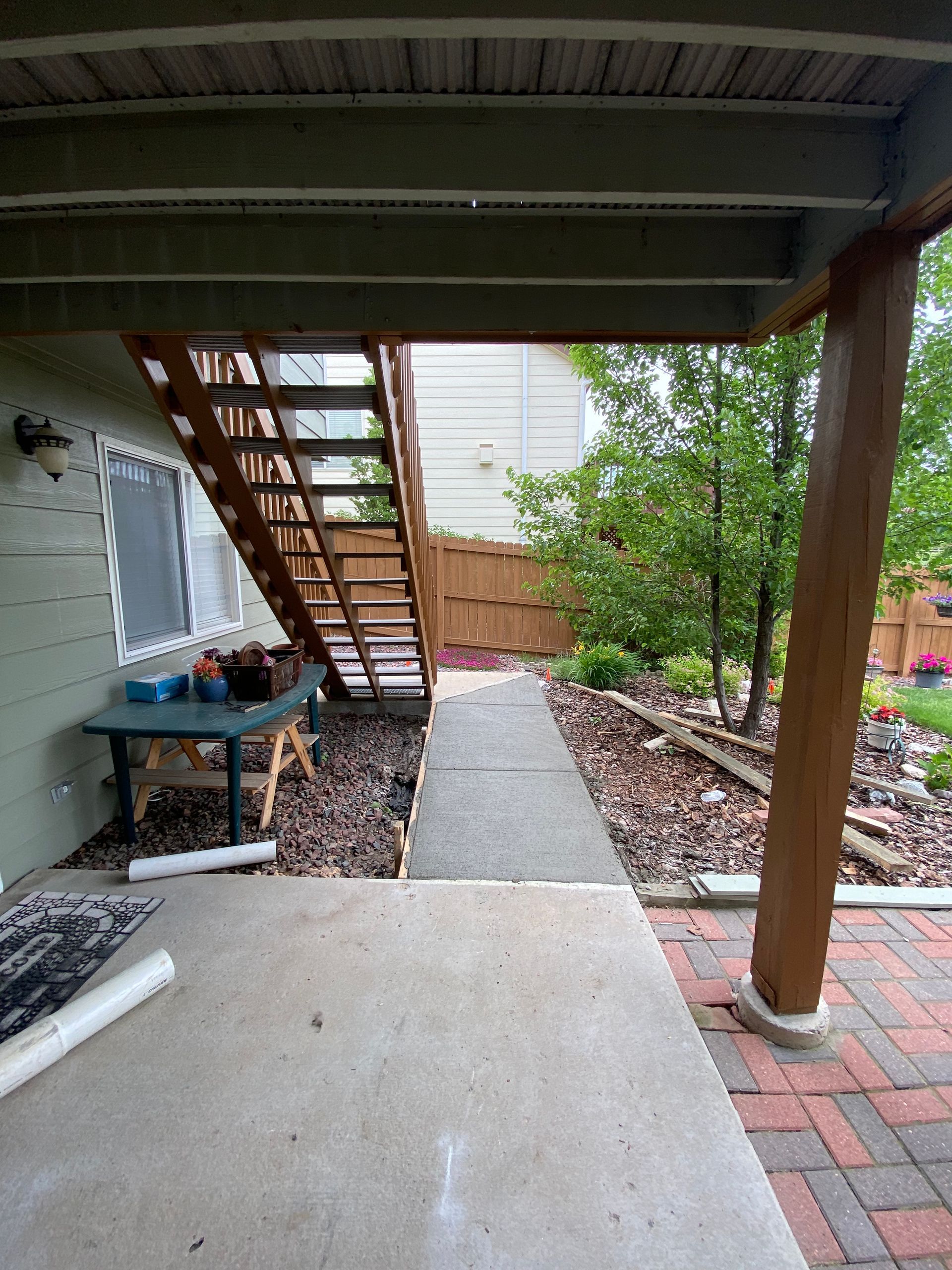 Underneath a deck: concrete patio, stairs, walkway, landscaped yard. A wooden post on the right.