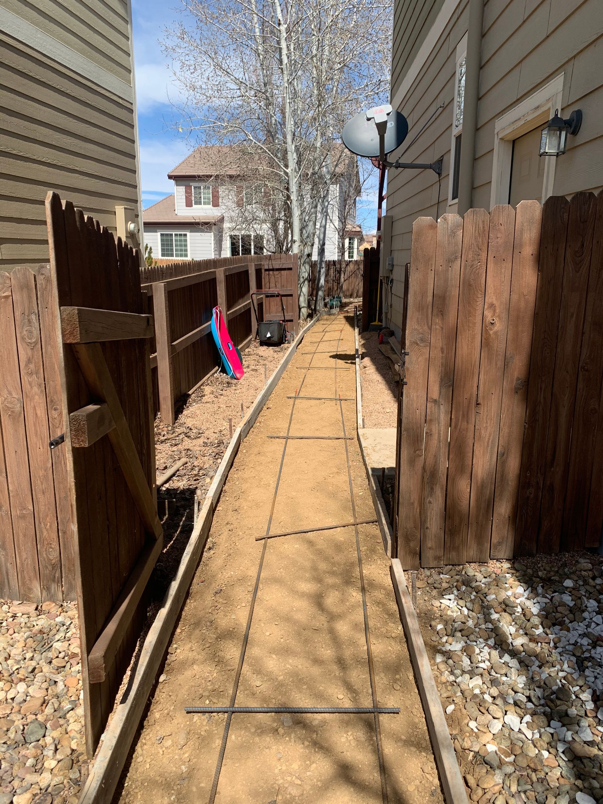 A narrow dirt walkway between brown fences and a building.