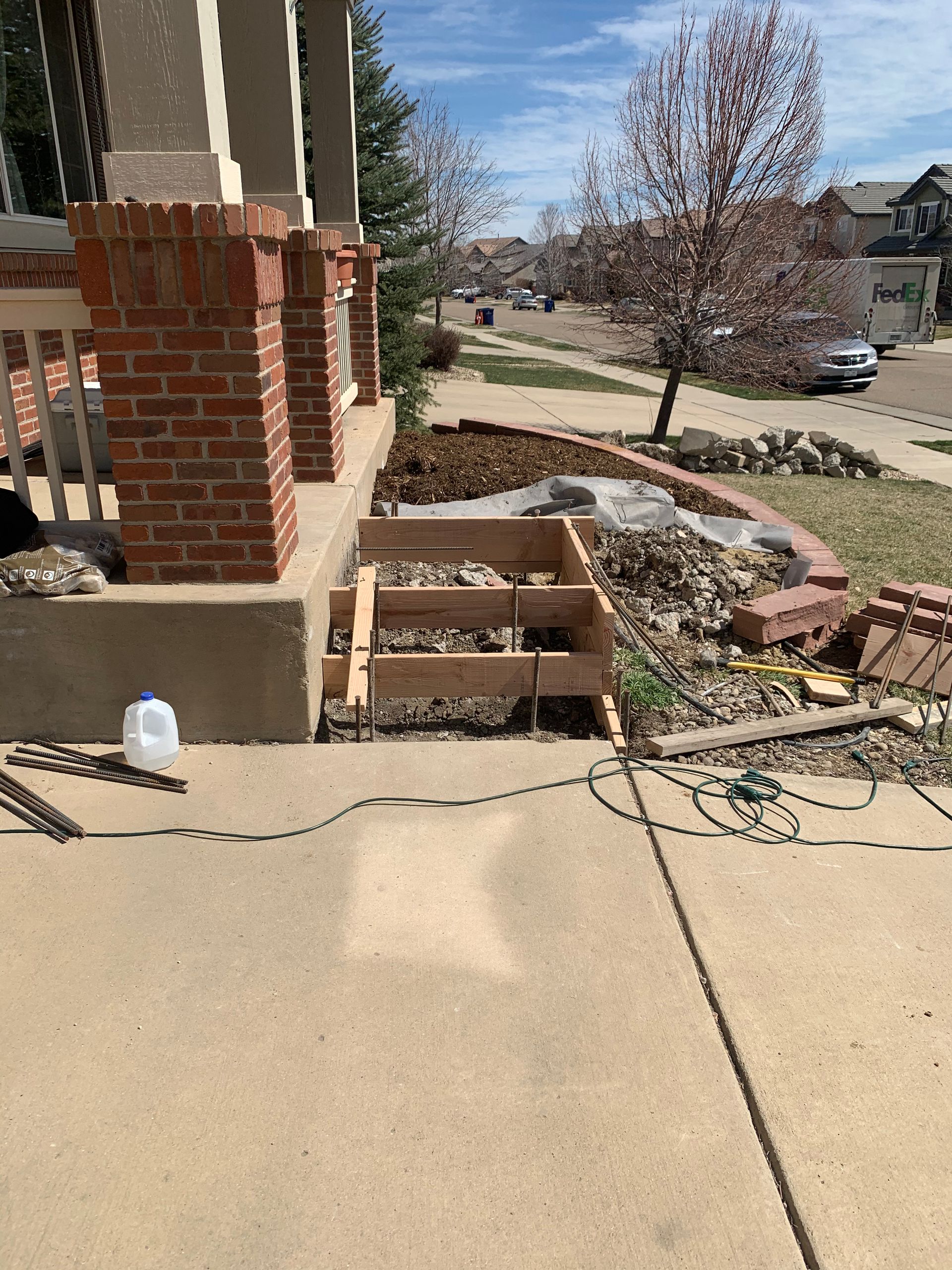 Exterior view of a house with concrete steps under construction. Wooden forms, bricks, and landscaping visible.